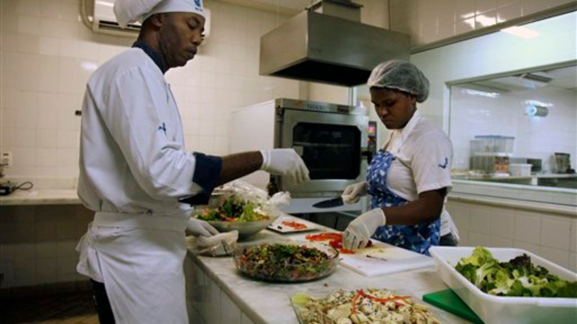 In this May 6, 2016 photo, cooks prepare meals during one of many food-testing exercises of the Olympic menu in Rio de Janeiro, Brazil. Diners will choose from five different buffets: Brazilian, Asian, International, Pasta and Pizza, Halal and Kosher, and everyone gets to dig into 40 varieties of Brazil's exotic fruits like caju, acai, carambola, caqui, goiaba and maracuja.
