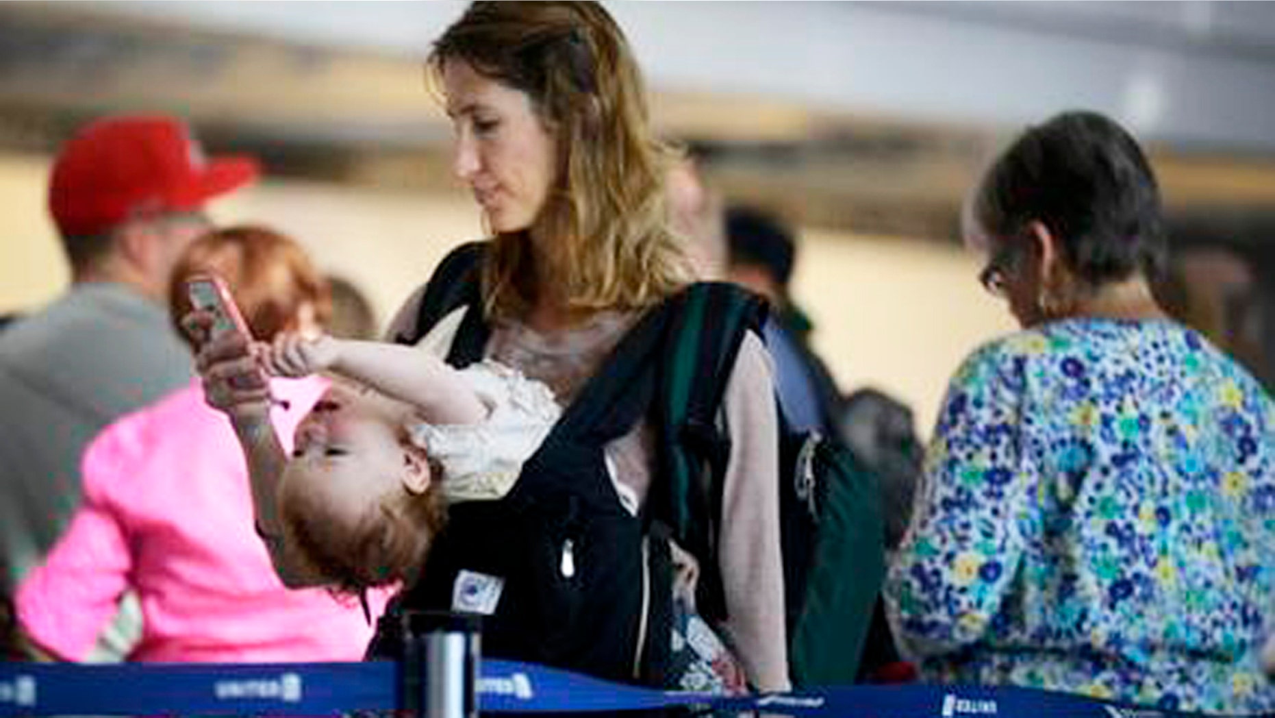 Ann Walden checks her phone as 15-month-old daughter Delphine plays while waiting in line after their flight to Baton Rouge was delayed at O'Hare International Airport in Chicago. There are several ways to distract and soothe little ones when traveling by air.