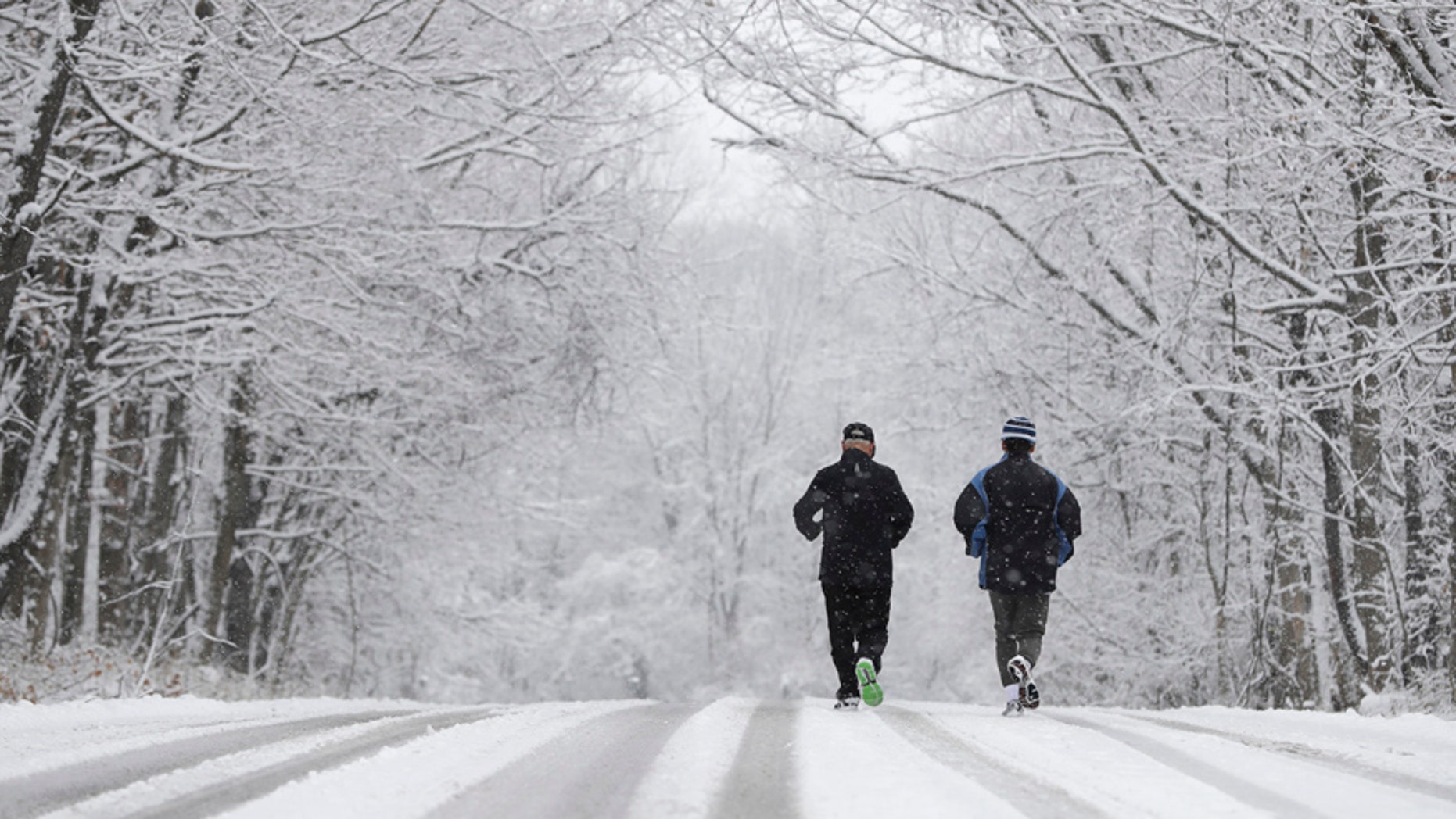 Ken Perry and Stan Ly go for a run in Eagle Creek Park as snow falls Tuesday, Dec. 13, 2016, in Indianapolis. (AP Photo/Darron Cummings)