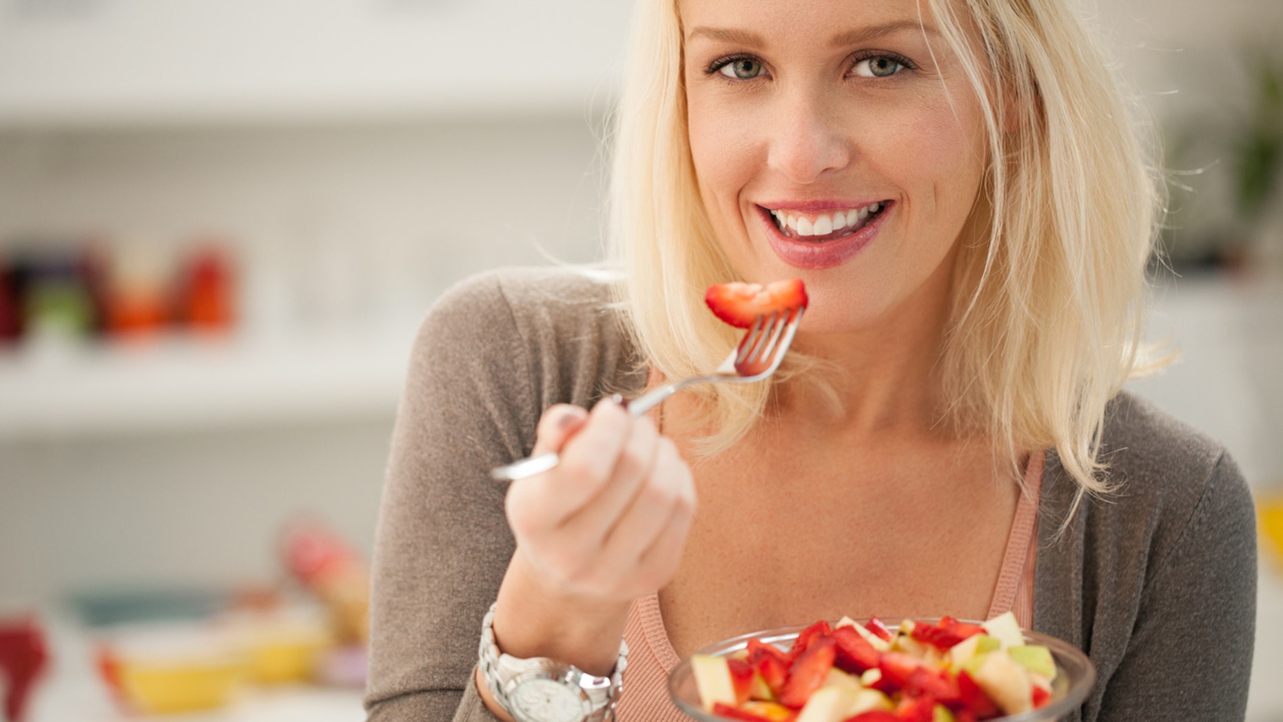 Smiling Caucasian woman eating a fresh fruit salad.