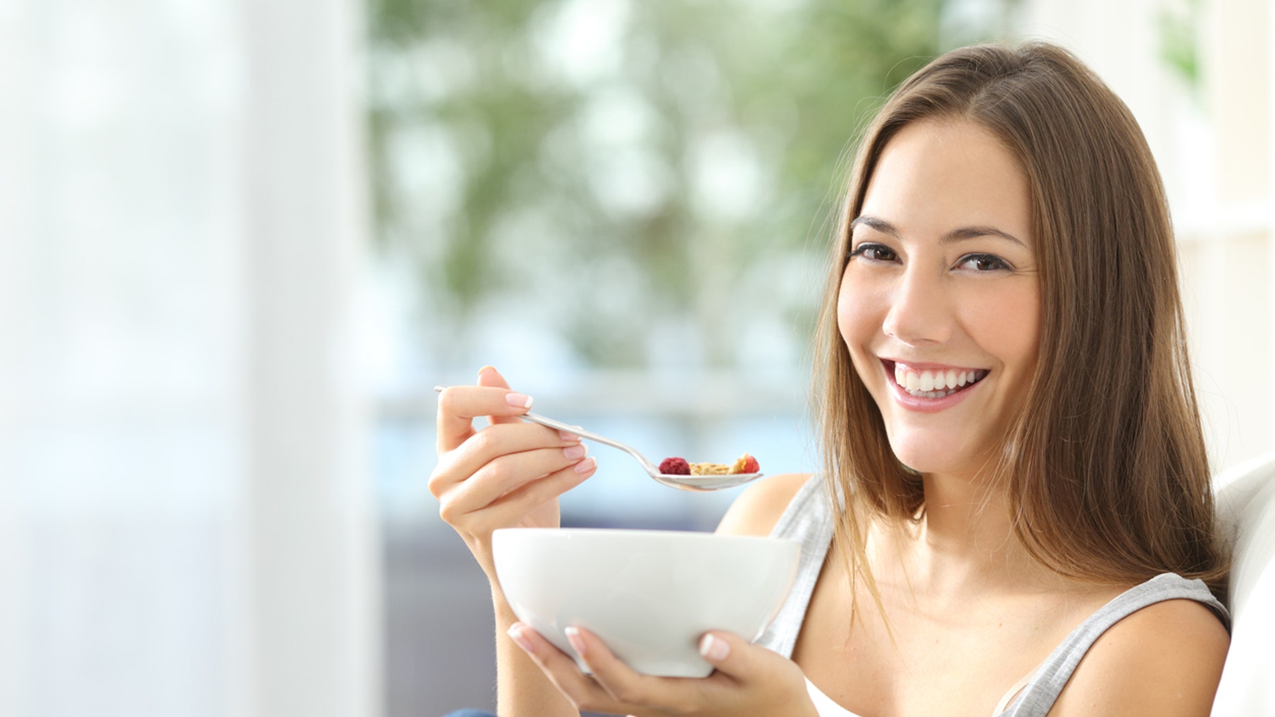 Casual happy woman dieting and eating cornflakes sitting on a couch at home