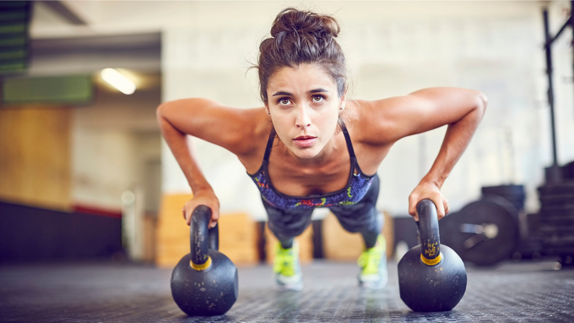 Focused athlete doing push-ups on kettlebells. Female is exercising in gym. Sporty woman is in health club.
