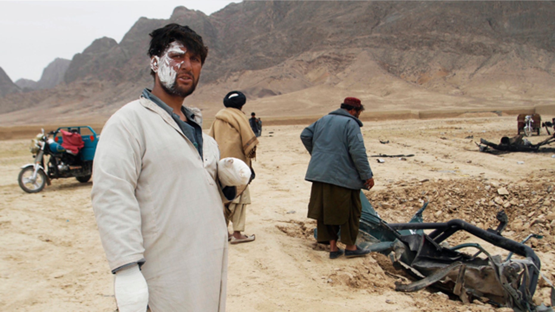 Feb. 27, 2011: A wounded Afghan man looks on as others examine the wreckage of a car after an explosion in the Arghandab district of Kandahar province, Afghanistan.