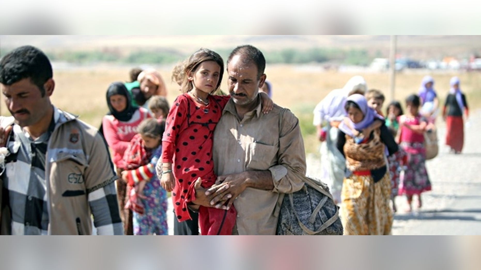 File photo: A displaced Yazidi Iraqi carries his daughter as they cross the Syrian border at Fishkhabour.