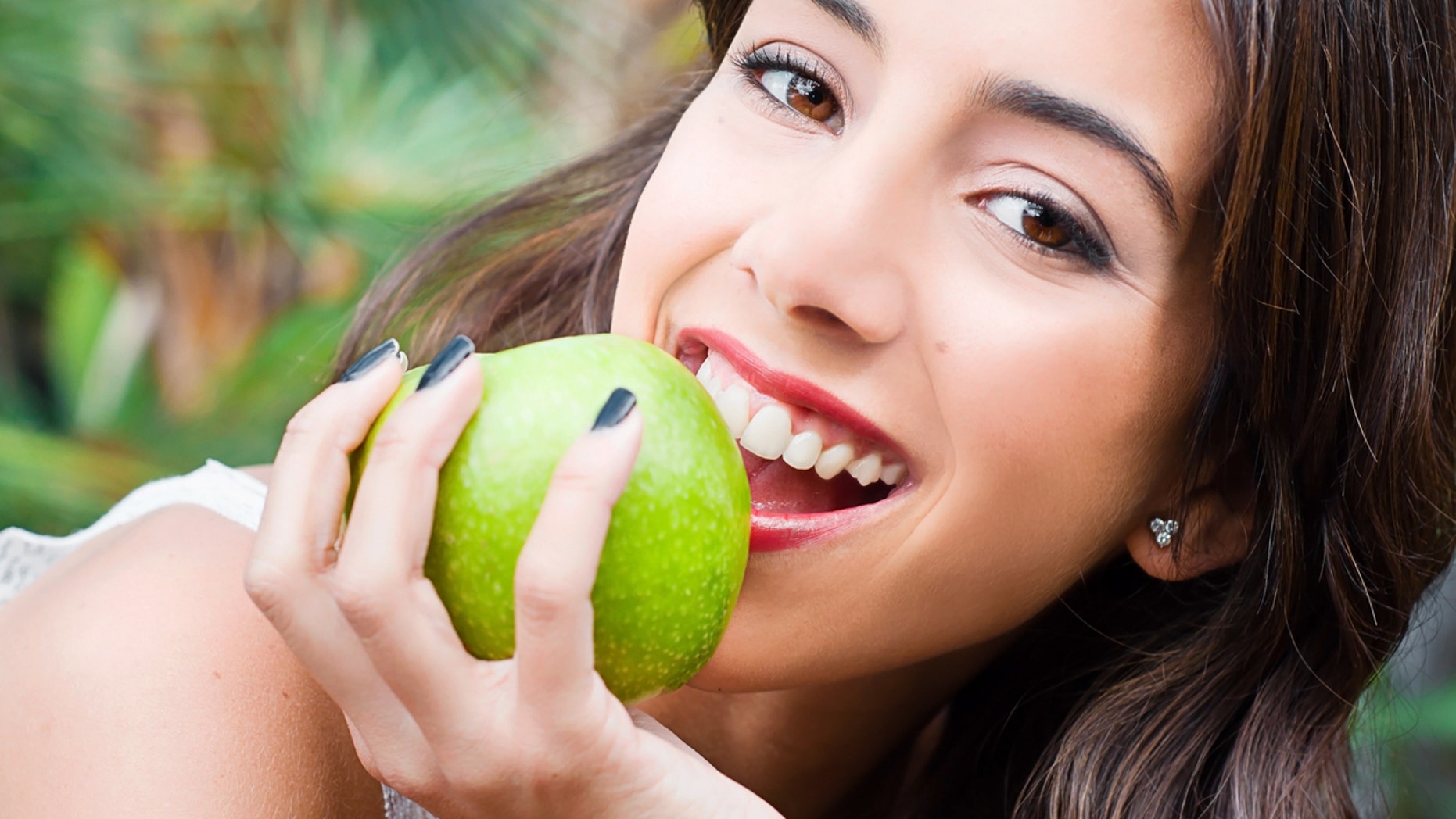 Young woman face eating a green apple and looking at the camera with a smile