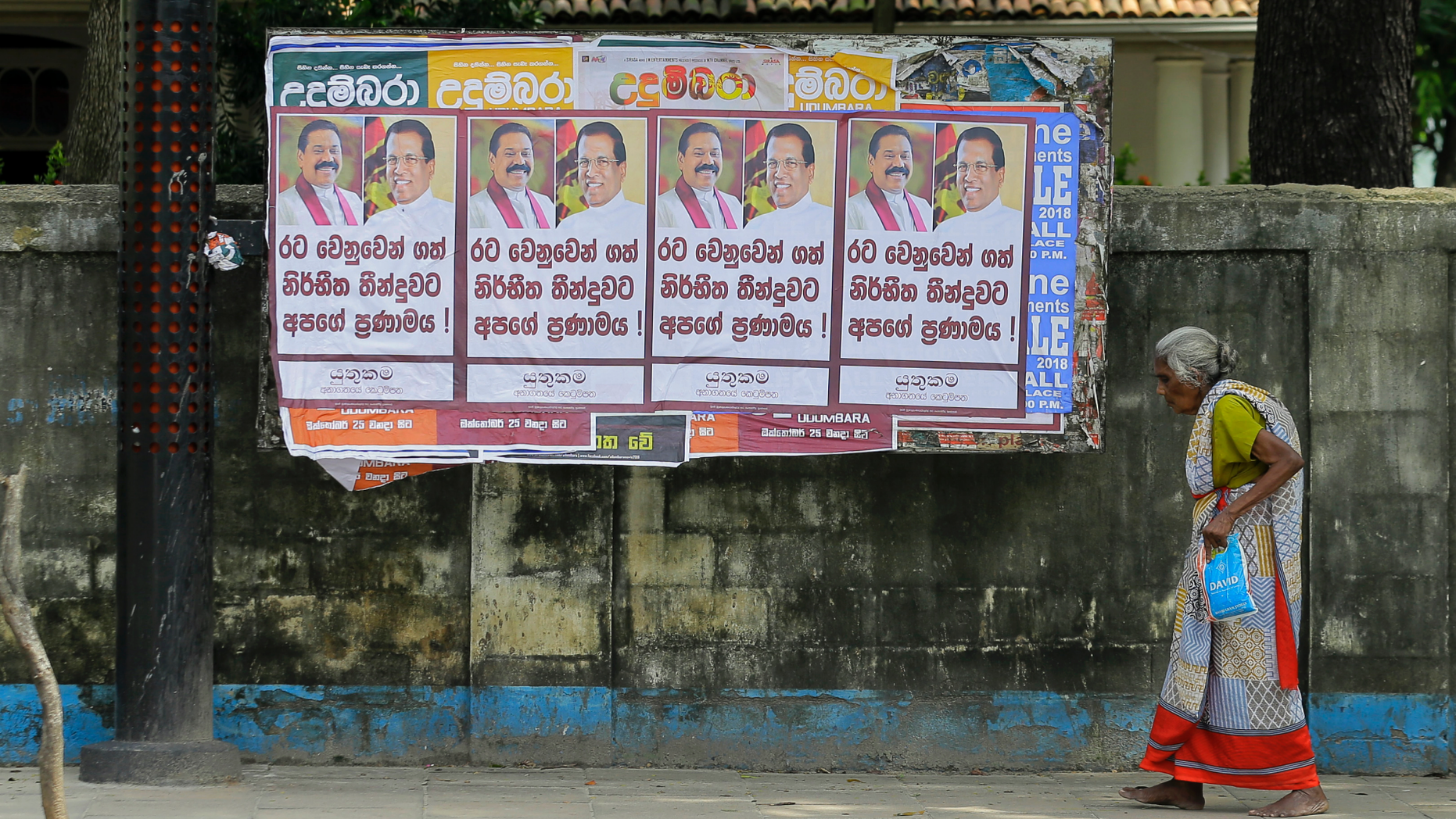 A Sri Lankan woman walks past a notice board covered with posters carrying portraits of President Maithripala Sirisena and newly appointed Prime Minster Mahinda Rajapaksa at a street in Colombo, Sri Lanka, Sunday, Oct. 28, 2018. Sri Lanka's president suspended Parliament even as the prime minister he fired the previous day claimed he has majority support, adding to a growing political crisis in the South Asian island nation. Posters read " Our respect for the decision took on behalf of the country." (AP Photo/Eranga Jayawardena)