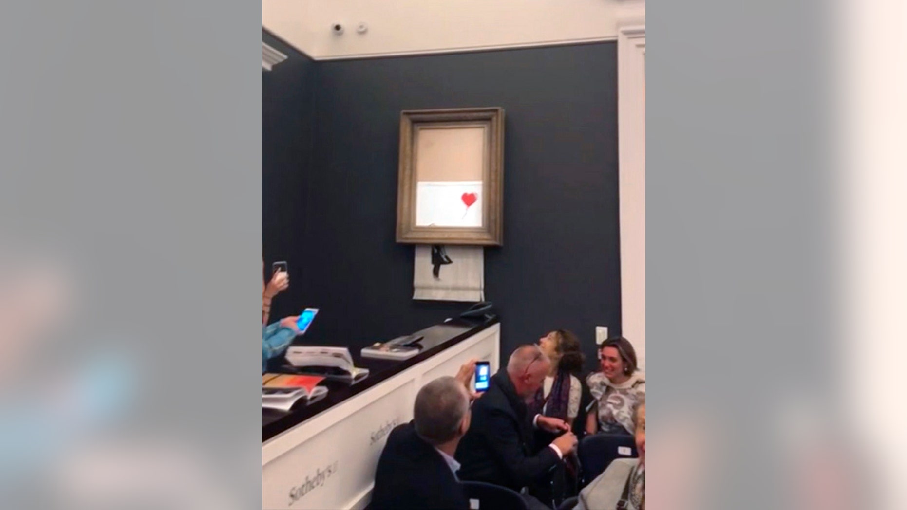 People watch as the spray-painted canvas "Girl with Balloon" by the artist Banksy self-destructs at Sotheby's, in London Oct. 5, 2018.