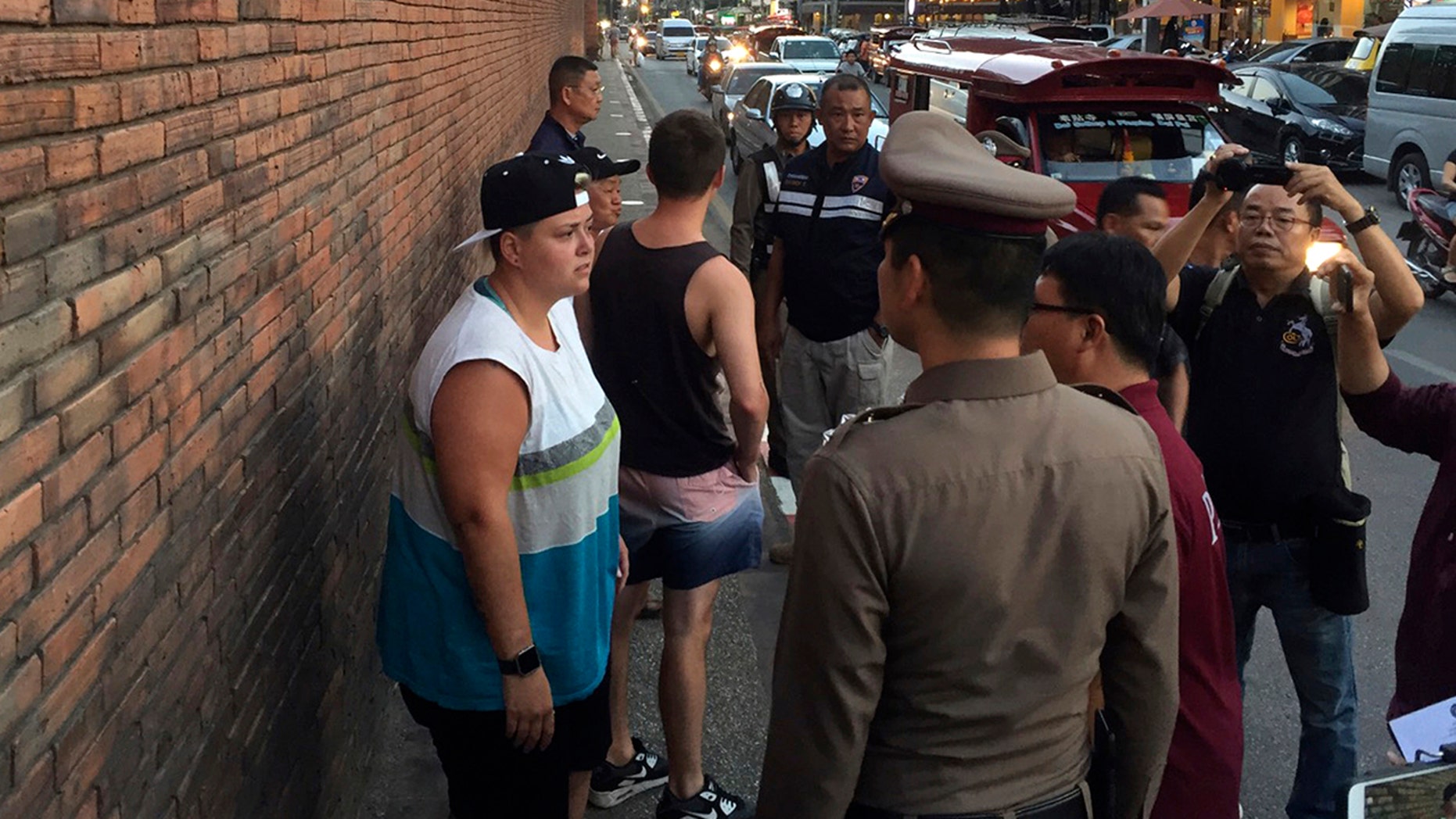 In this Thursday, Oct. 18, 2018, photo, Canadian Brittney Lorretta Katherine Schneider, left, and British Furlong Lee, second left, stand in front of Tha Pae Gate in Chiang Mai province, northern Bangkok, Thailand. They face up to 10 years in prison on charges of spraying paint on an ancient wall in northern Thailand, police said Friday. (Chiang Mai News via AP)