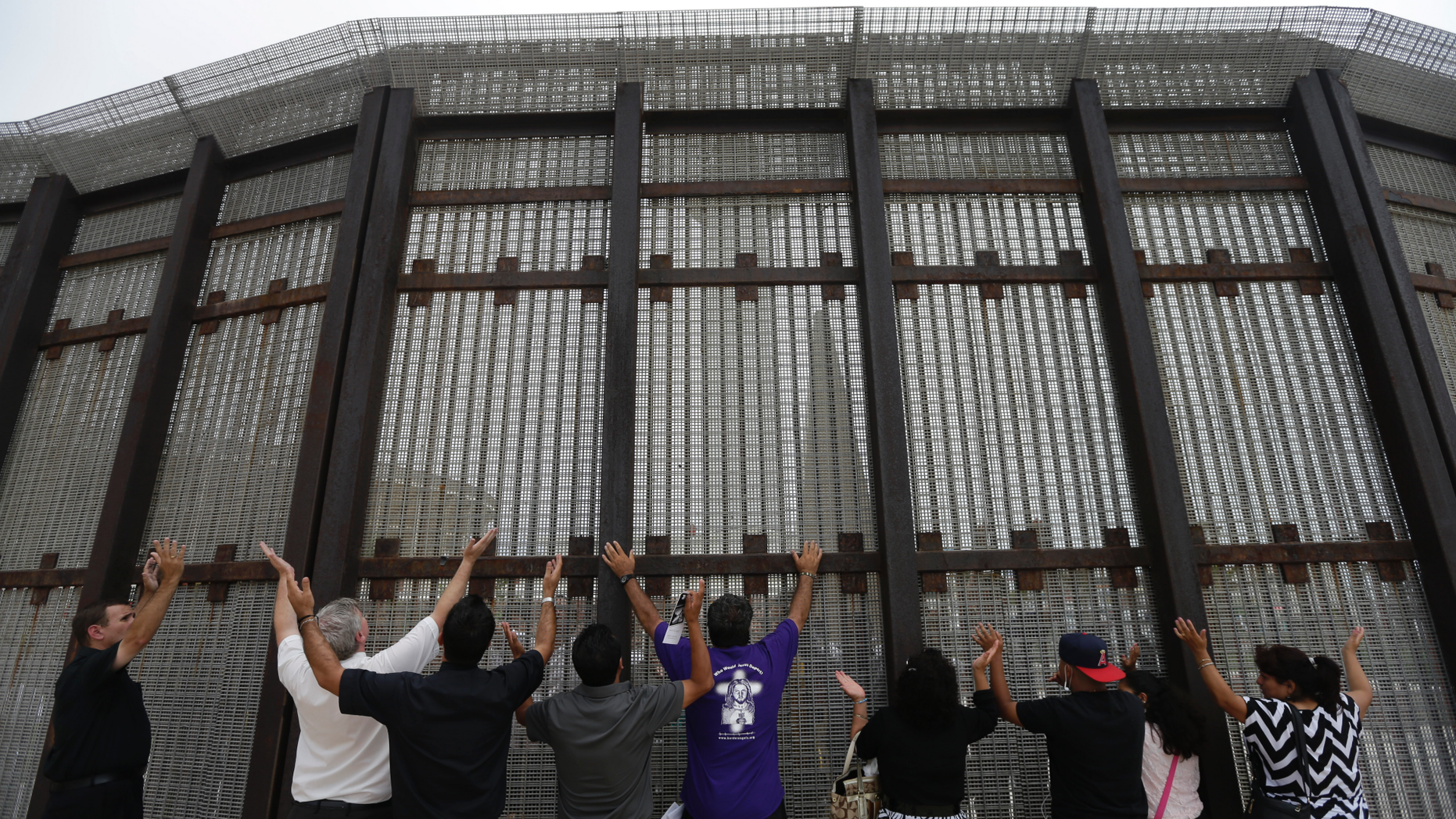 FILE - In this July 14, 2013, file photo, pastors and others raise their arms on the San Diego side of a border fence during a cross-border Sunday religious service with others on the Tijuana, Mexico side of the fence. The Tijuana and San Diego border crossing is the world's busiest land border crossing, but also now sees relatively few illegal crossings. (AP Photo/ Gregory Bull, File)