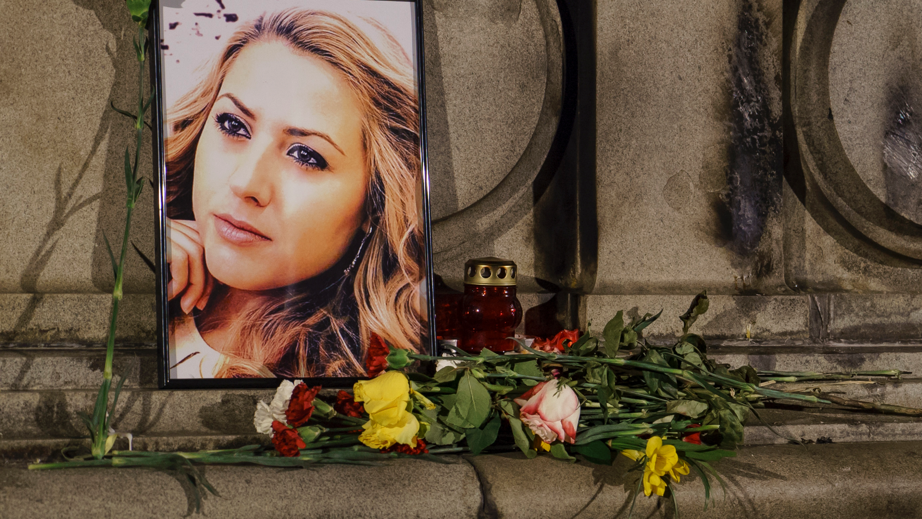 A portrait of slain television reporter Viktoria Marinova is placed on the Liberty Monument next to flowers and candles during a vigil in Ruse, Bulgaria, Tuesday, Oct. 9, 2018. Bulgarian police are investigating the rape, beating and slaying of Marinova, whose body was dumped near the Danube River after she reported on the possible misuse of European Union funds in Bulgaria. Authorities discovered the body of 30-year-old Viktoria Marinova on Saturday in the northern town of Ruse near the Romanian border. One Bulgarian media site demanded an EU investigation, fearing that Bulgarian officials were complicit in the corruption. (AP Photo/Filip Dvorski)