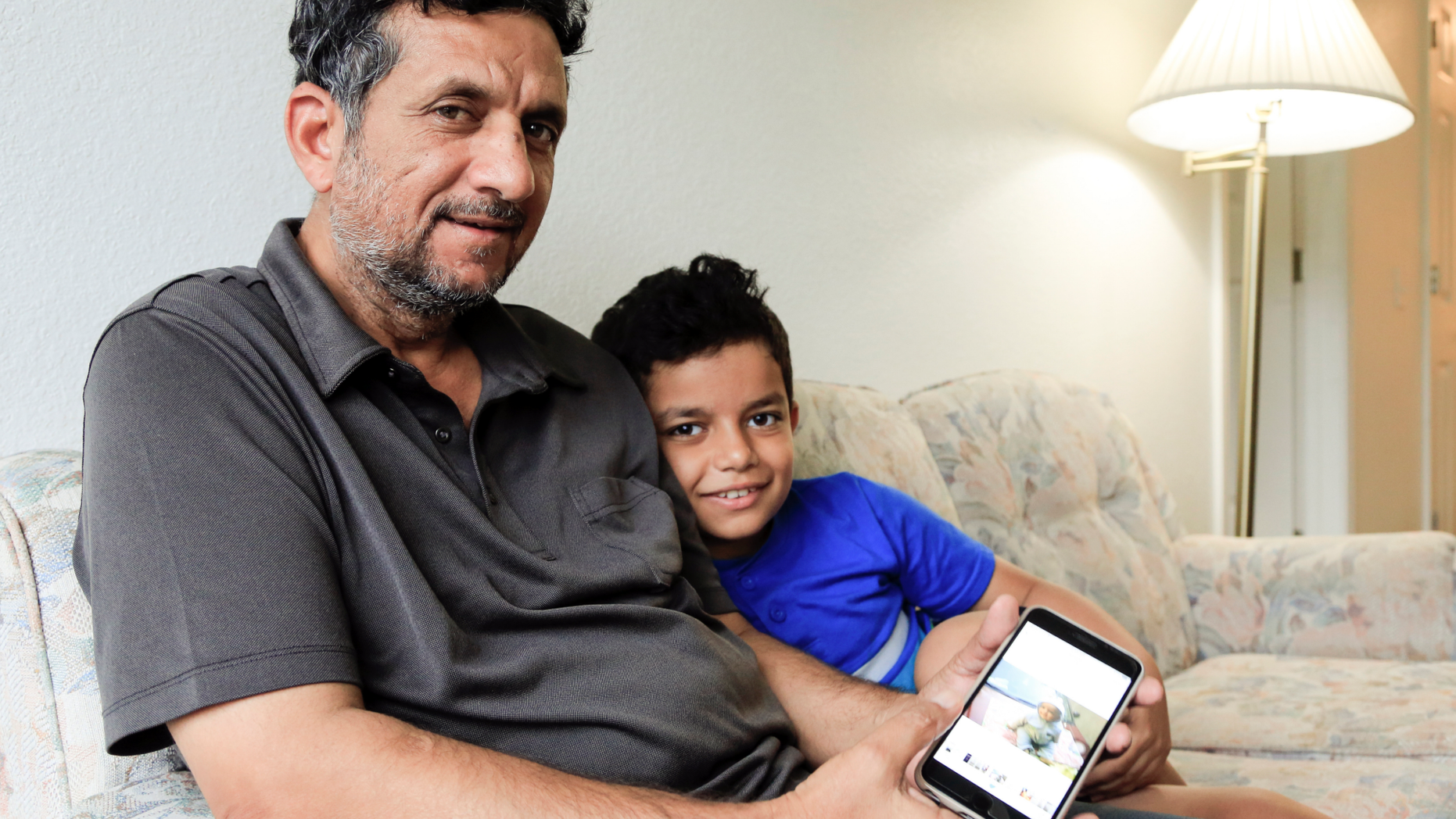 In this Sept. 29, 2018 photo, Hadi Mohammed sits with his 9 year old son Mohammed Ghaleb, as he displays a photo of his son as a baby in Baghdad, in their Lincoln, Neb. apartment. Death threats drove Hadi Mohammed out of Iraq and to a small apartment in Nebraska, where he and his two young sons managed to settle as refugees. But the danger hasn’t been enough to allow his wife to join them. (AP Photo/Nati Harnik)