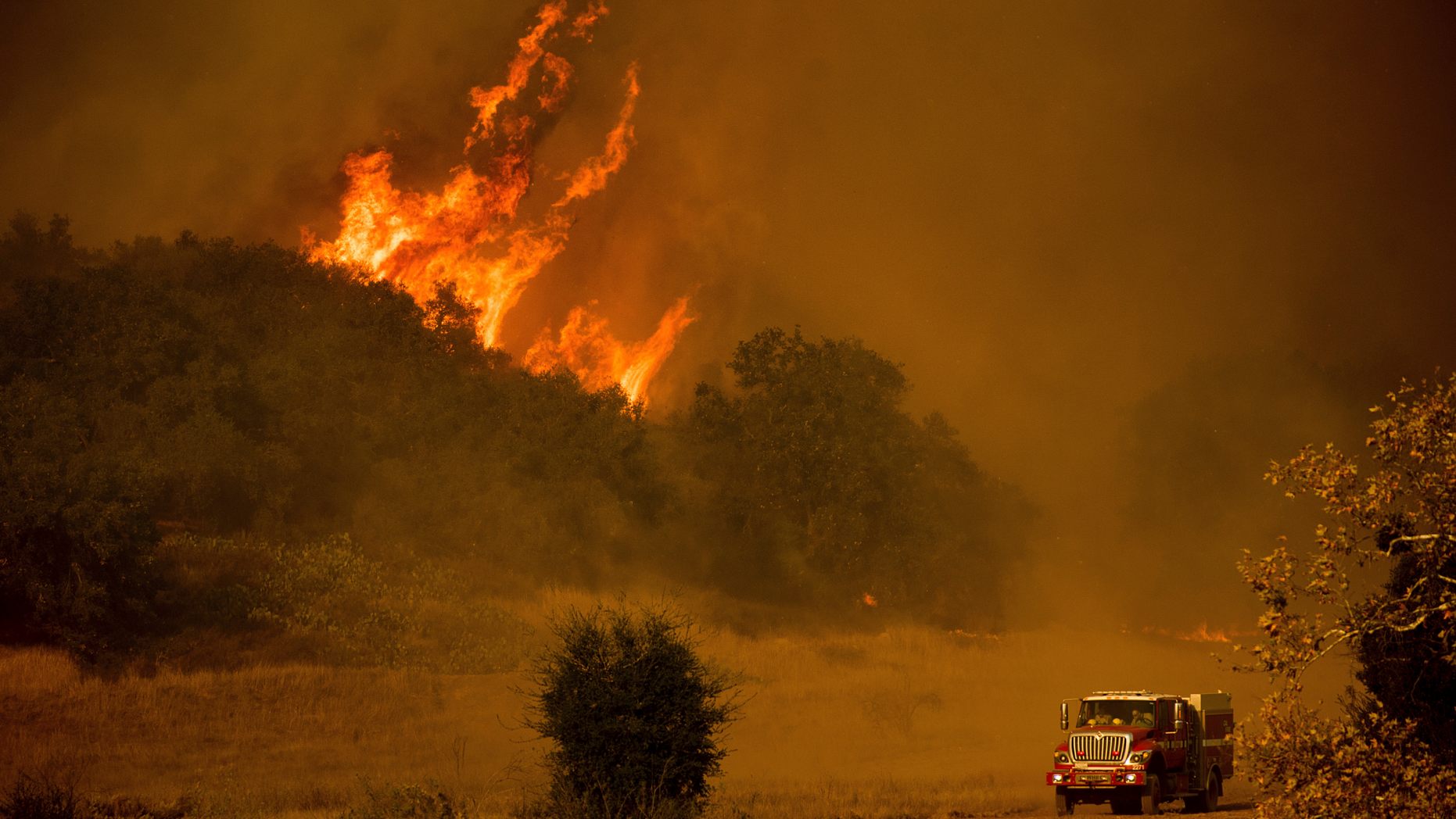 FILE - In this Dec. 9, 2017 file photo, a fire engine passes flames as a wildfire burns along Santa Ana Road near Ventura, Calif. Southern California Edison said Tuesday, Oct. 30, 2018, its equipment likely sparked one of two ignition points for Thomas fire, a wildfire that tore through California's central coast last year. (AP Photo/Noah Berge, File)