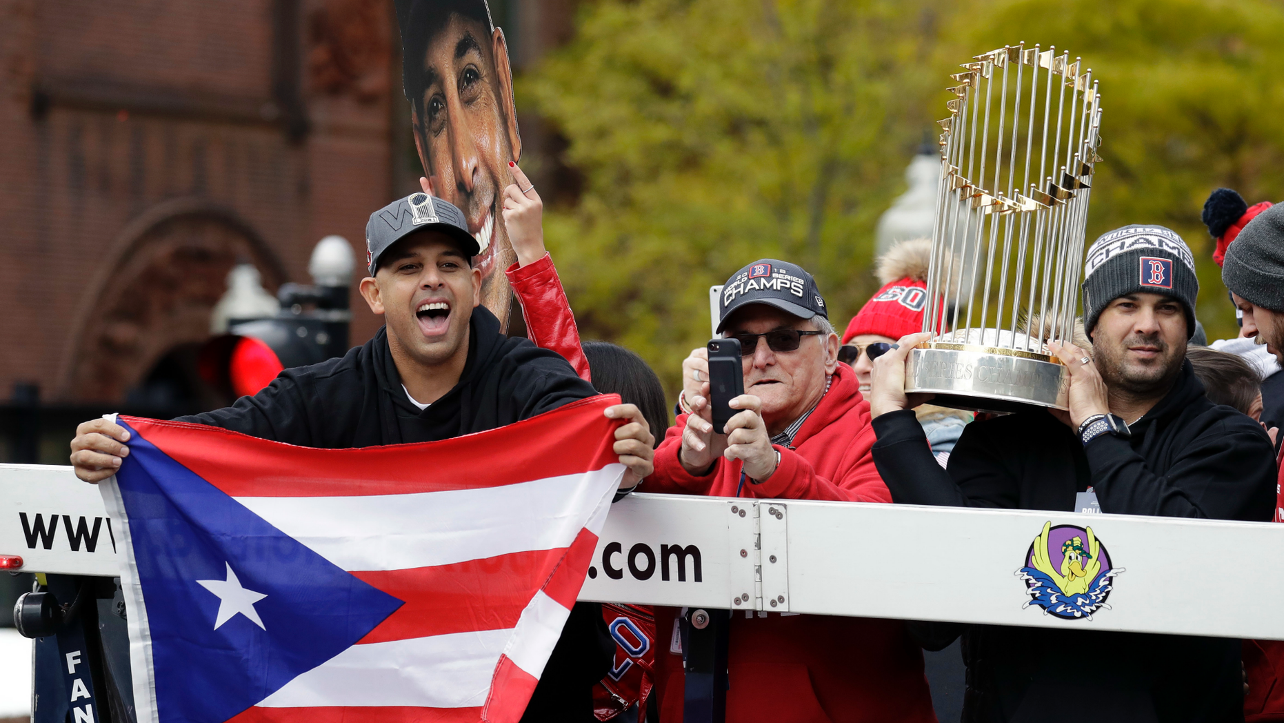 Boston Red Sox manager Alex Cora, left, waves the flag of Puerto Rico as coach Ramon Vazquez holds the championship trophy during a parade to celebrate the team's World Series championship over the Los Angeles Dodgers, Wednesday, Oct. 31, 2018, in Boston. (AP Photo/Elise Amendola)