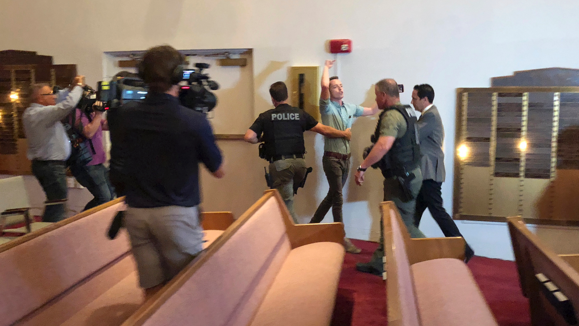 Police officers escort protester Jacob Engels from a Florida synagogue Thursday, Oct. 25, 2018, in Plantation, Fla., before a speech by Democratic gubernatorial candidate Andrew Gillum. Engel shouted Gillum is "a radical Jew hater who supports mob violence" as he was removed by Plantation, Florida, police officers. Gillum later told the crowd that support for Israel should be bipartisan and that accusations he is an anti-Semite are false. (AP Photo/Terry Spencer)