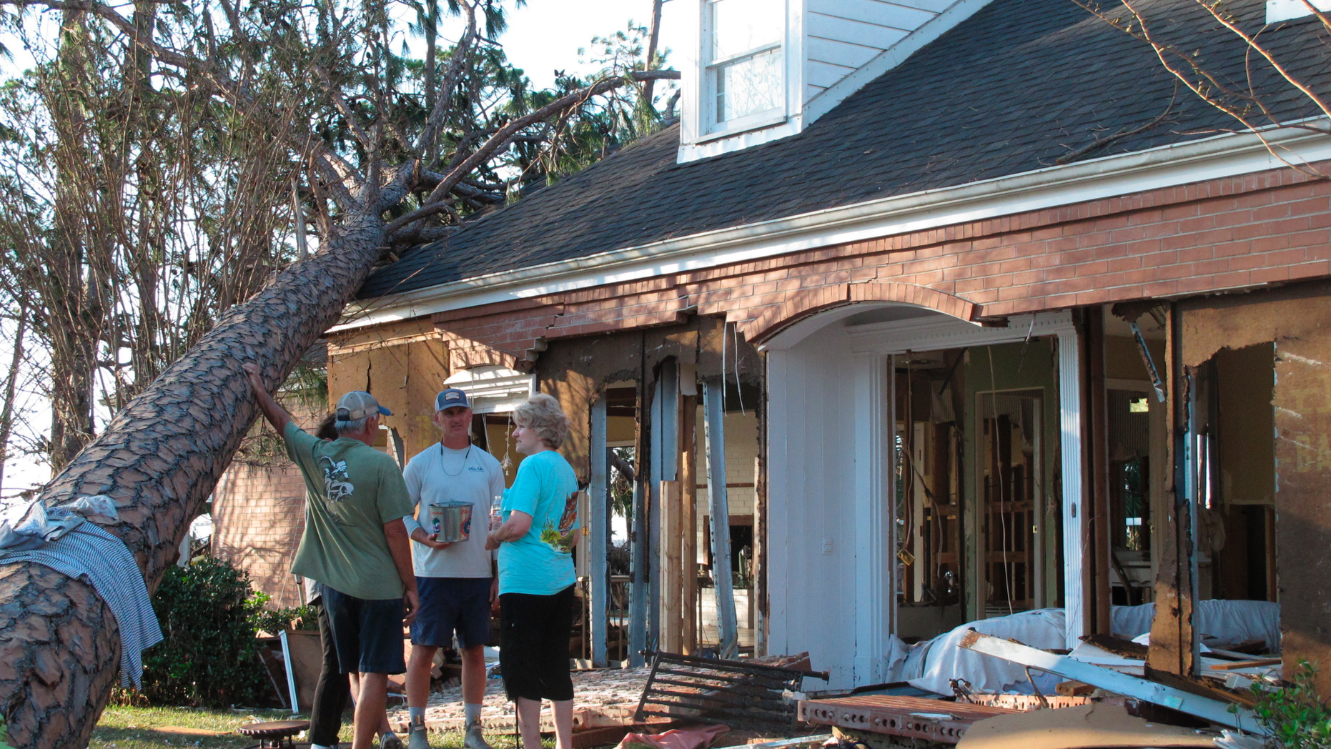 Rex Buzzett, far left, his son Josh Buzzett and neighbor Hilda Duren stand outside the Buzzett’s home, Thursday, Oct. 11, 2018, that was gutted by a storm surge in Port St. Joe, Fla. Hurricane Michael devastated several homes overlooking the Gulf of Mexico in Port St. Joe, while largely sparing residents of the neighboring Gulf community of Apalachicola. (AP Photo/Russ Bynum)