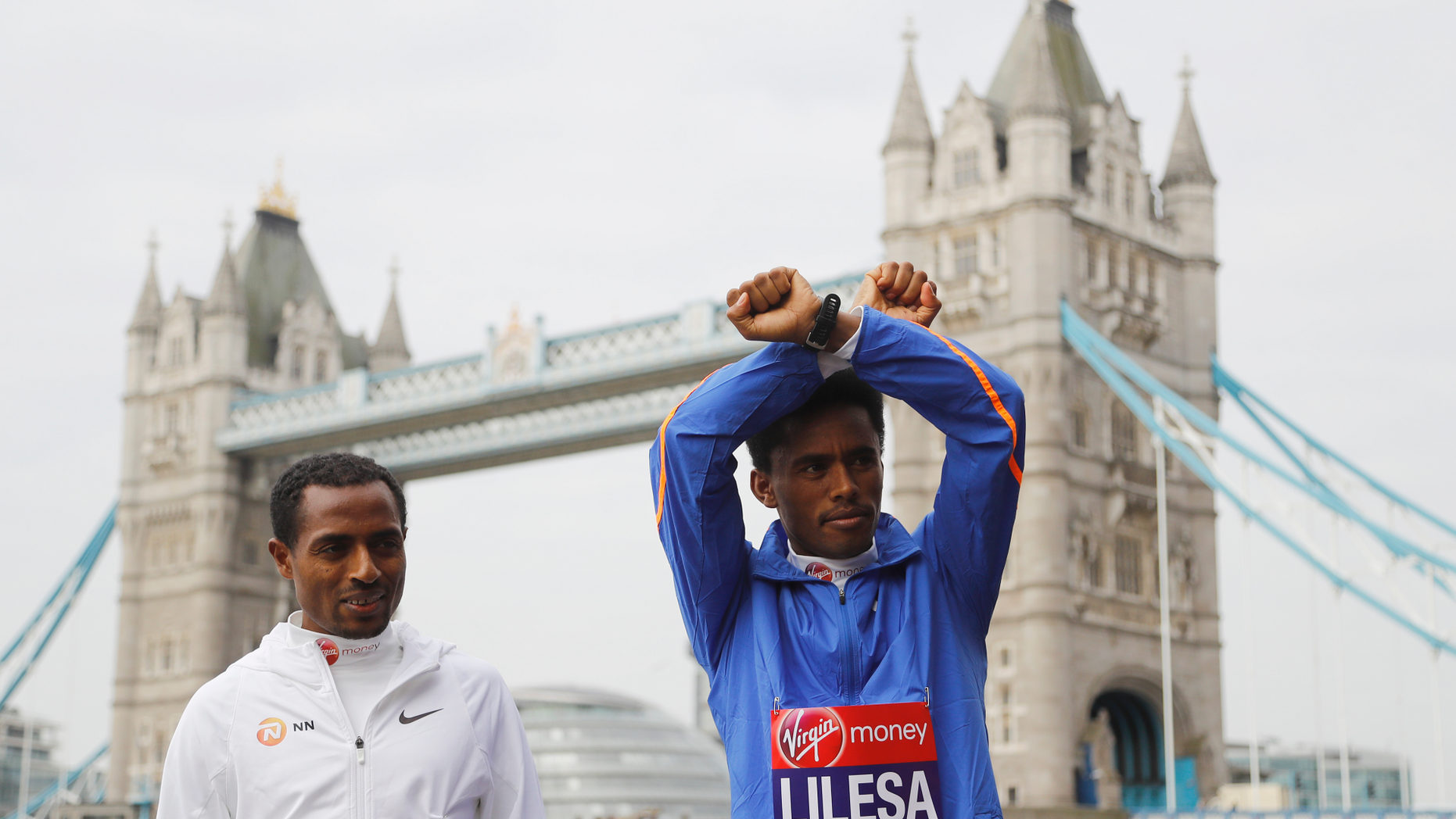 FILE - In this Thursday, April 20, 2017 file photo, Feyisa Lilesa, right, and Kenenisa Bekele from Ethiopia stand in front of the Tower Bridge in London. The Ethiopian marathon runner who made global headlines with an anti-government gesture at the Rio Olympics finish line has returned from exile, after sports officials assured him he will not face prosecution. Feyisa Lilesa's return from the United States on Sunday, Oct. 21, 2018 comes several months after a reformist new prime minister took office and announced sweeping reforms. (AP Photo/Frank Augstein, file)