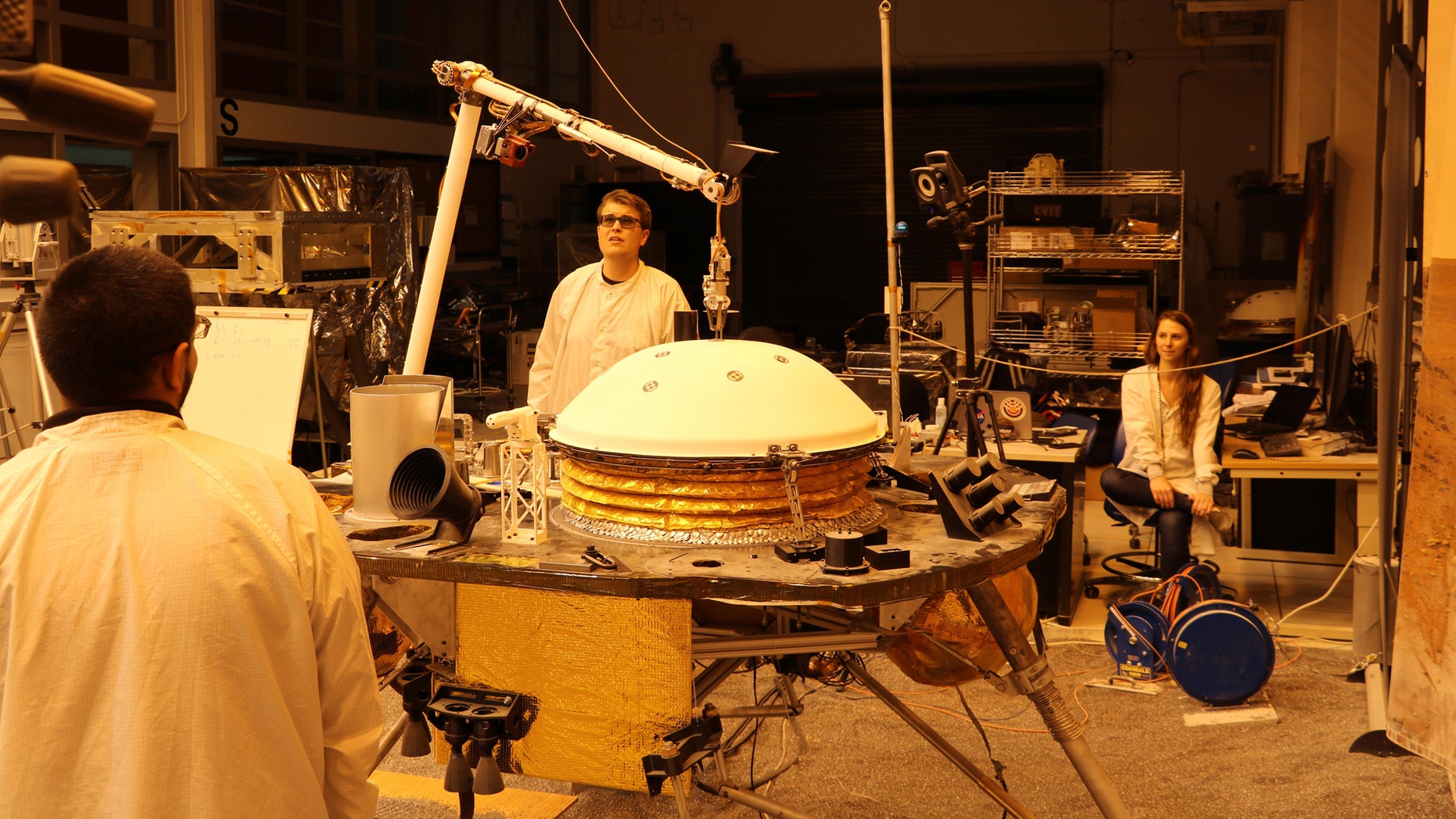 La mission InSight de la NASA teste une version d'ingénierie du bras robotique du vaisseau spatial dans un environnement similaire à celui de la planète Mars au Jet Propulsion Laboratory de la NASA. Le grappin à cinq doigts au bout du bras robotique soulève le Wind and Thermal Shield, une protection pour le sismomètre InSight. Le test est effectué sous le rougeâtre 