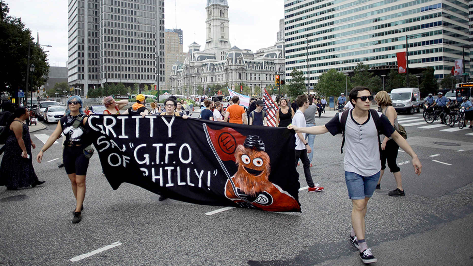 Demonstrators march through the Center City holding a banner with an image of the Philadelphia Flyers’ new mascot, Gritty, before a speech by President Trump at the National Electrical Contractors Convention on Tuesday.