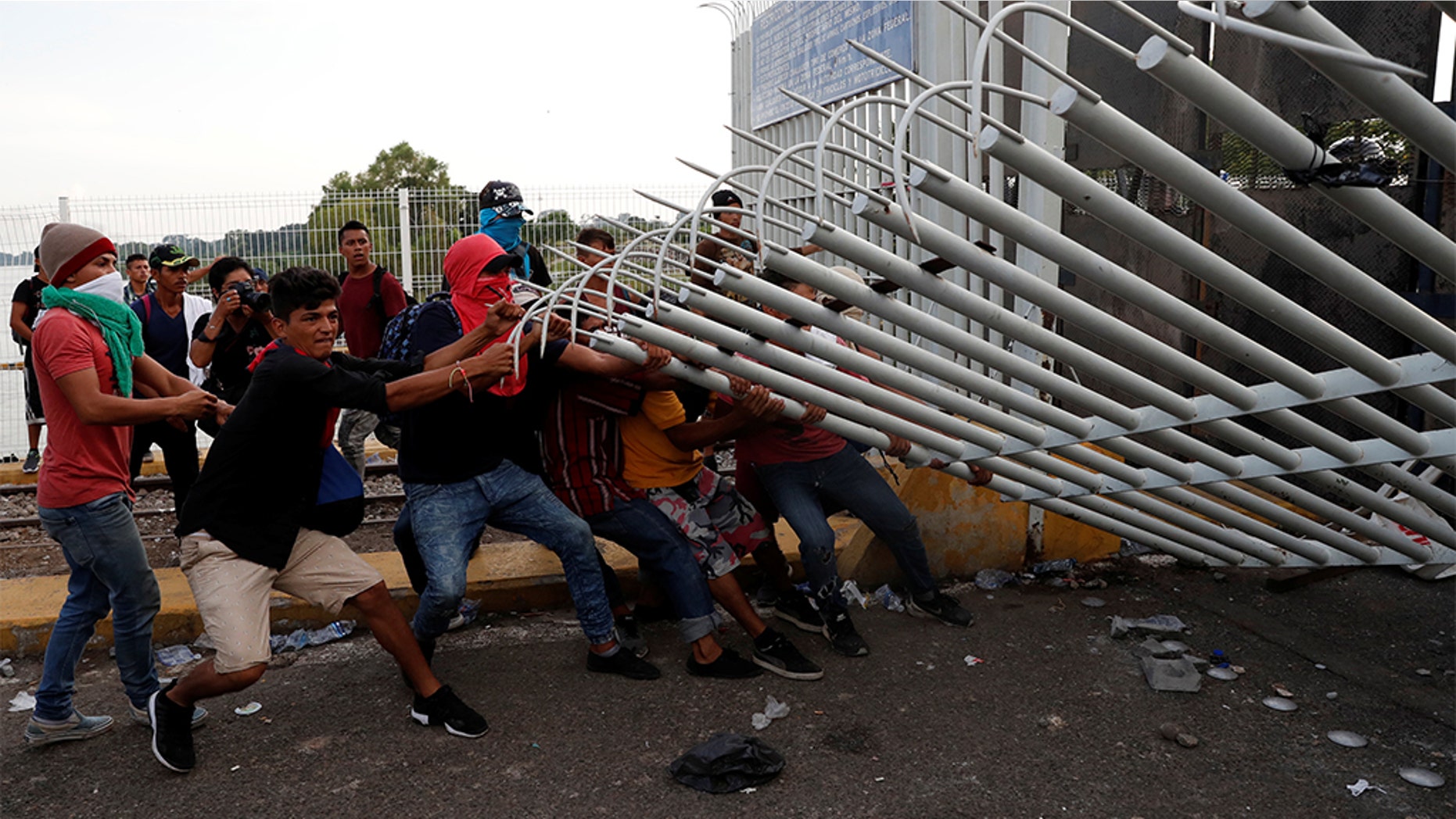 A group of men, part of a caravan of thousands of migrants from Central America en route to the U.S, pulling down a border gate with the intention to carry on their journey, in Tecun Uman, Guatemala.
