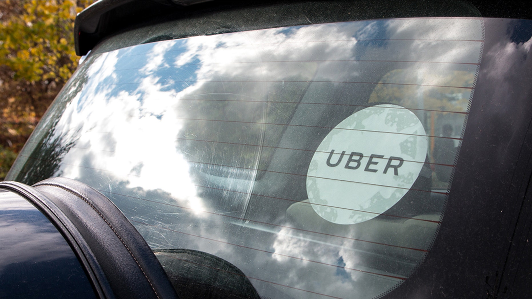 Rear window of a black Uber car with the white Uber sticker on the glass.