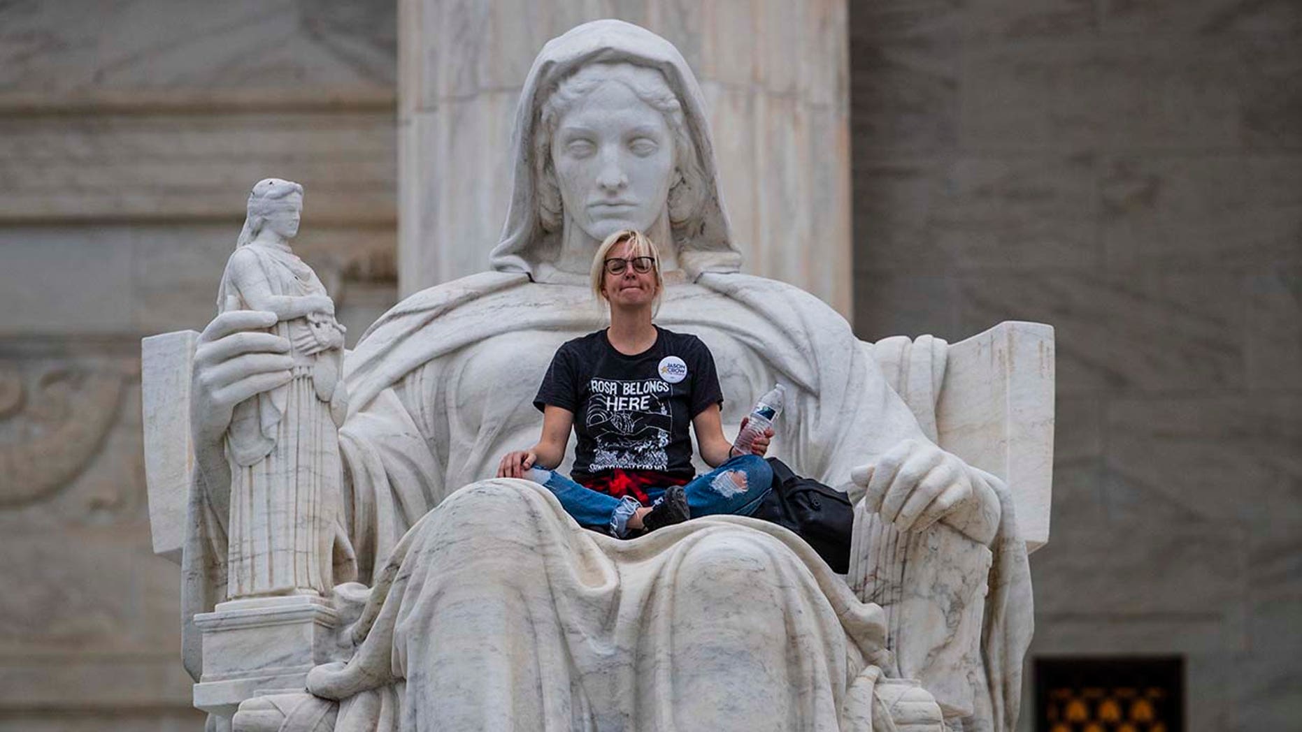 Jessica Campbell-Swanson an activist from Denver sits in the lap of a sculpture known as the Statue of Contemplation of Justice on the steps of the Supreme Court Building where she and others protested the confirmation of Brett Kavanaugh as the high cou