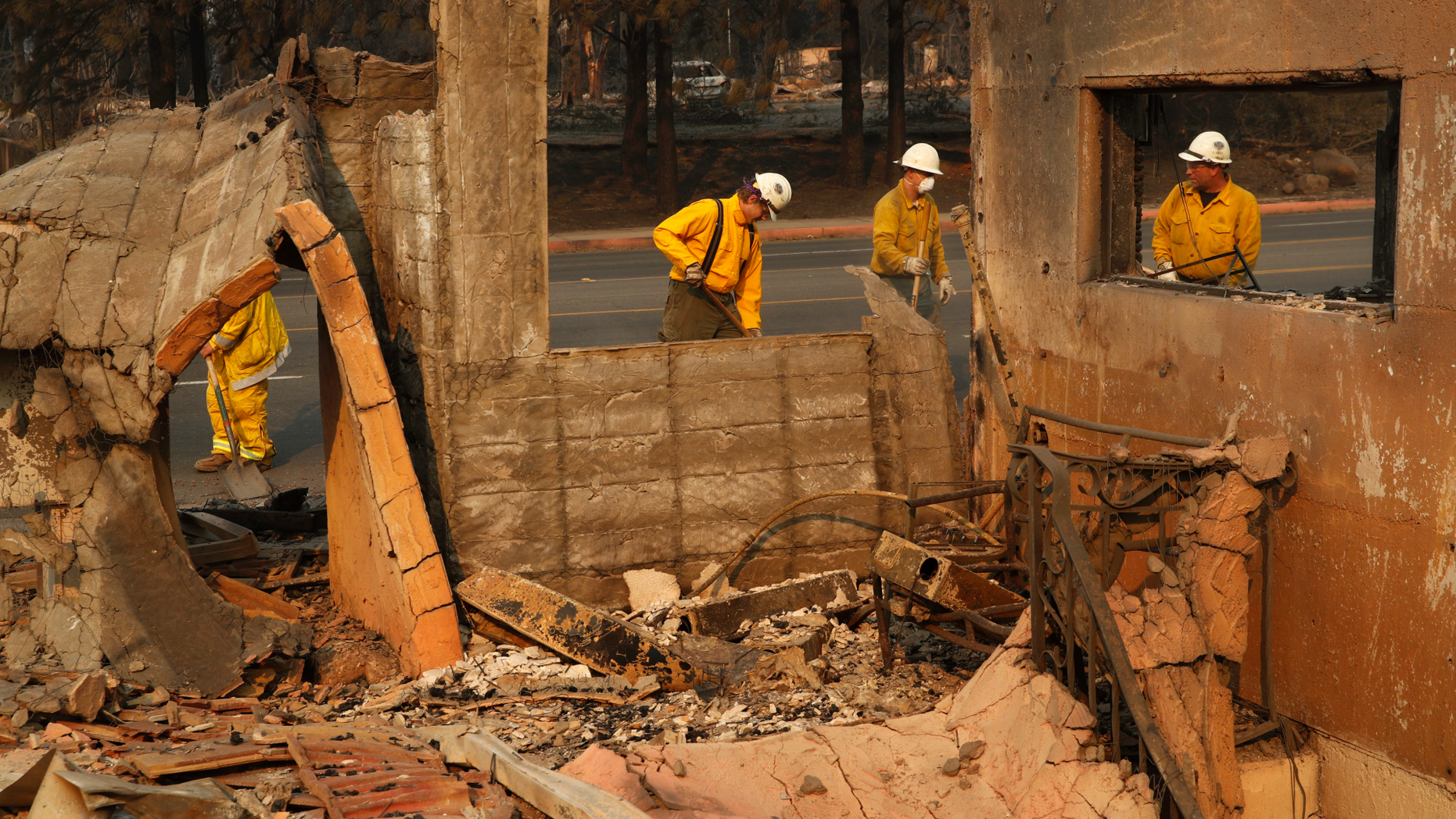 Fire crews clear rubble from the road near a building burned in the Camp Fire, Monday, Nov. 12, 2018, in Paradise, Calif. (AP Photo/John Locher)