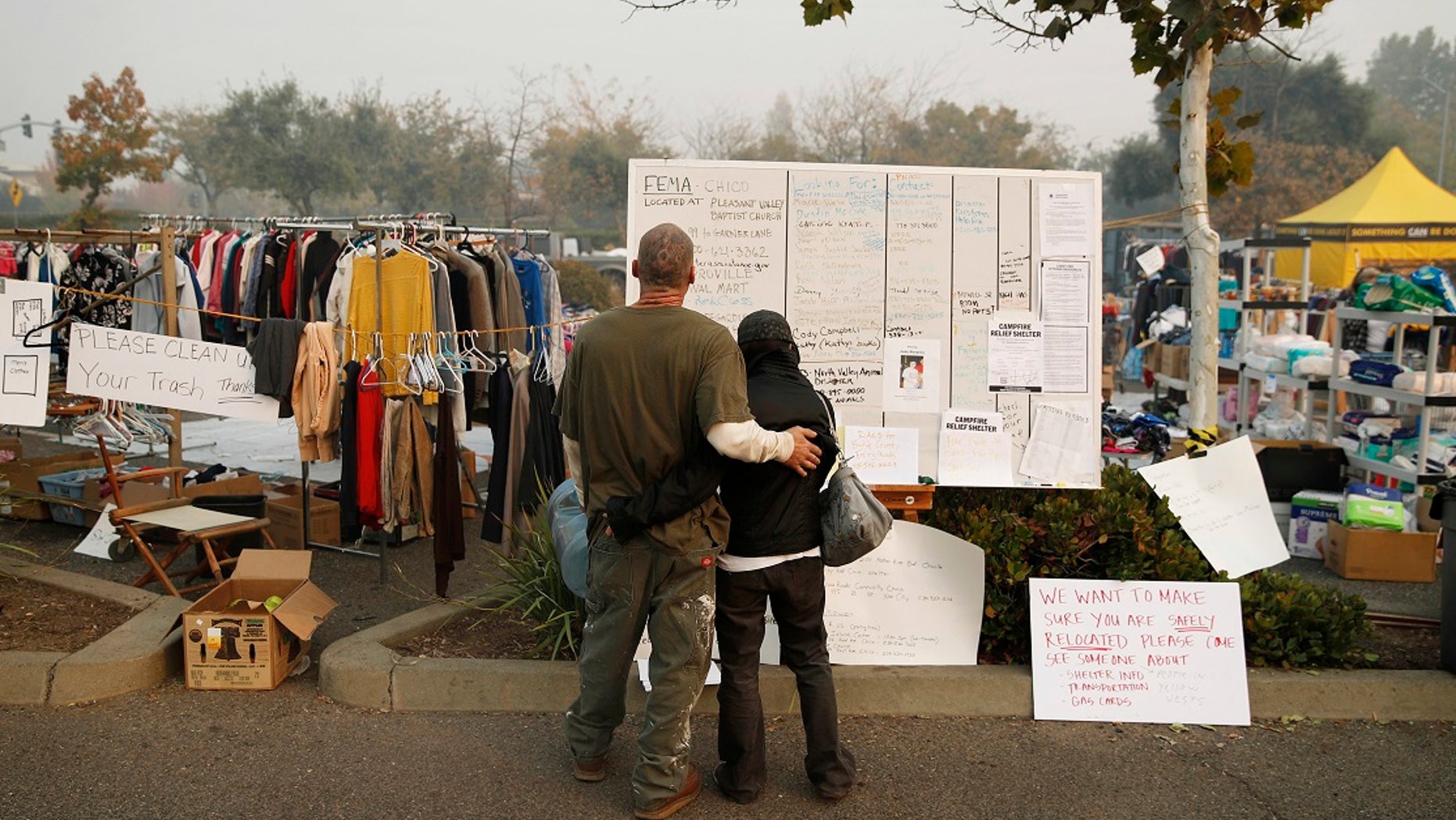 Tera Hickerson, right, and Columbus Holt embrace as they look at a board with information for services at a makeshift encampment outside a Walmart store for people displaced by the Camp Fire.