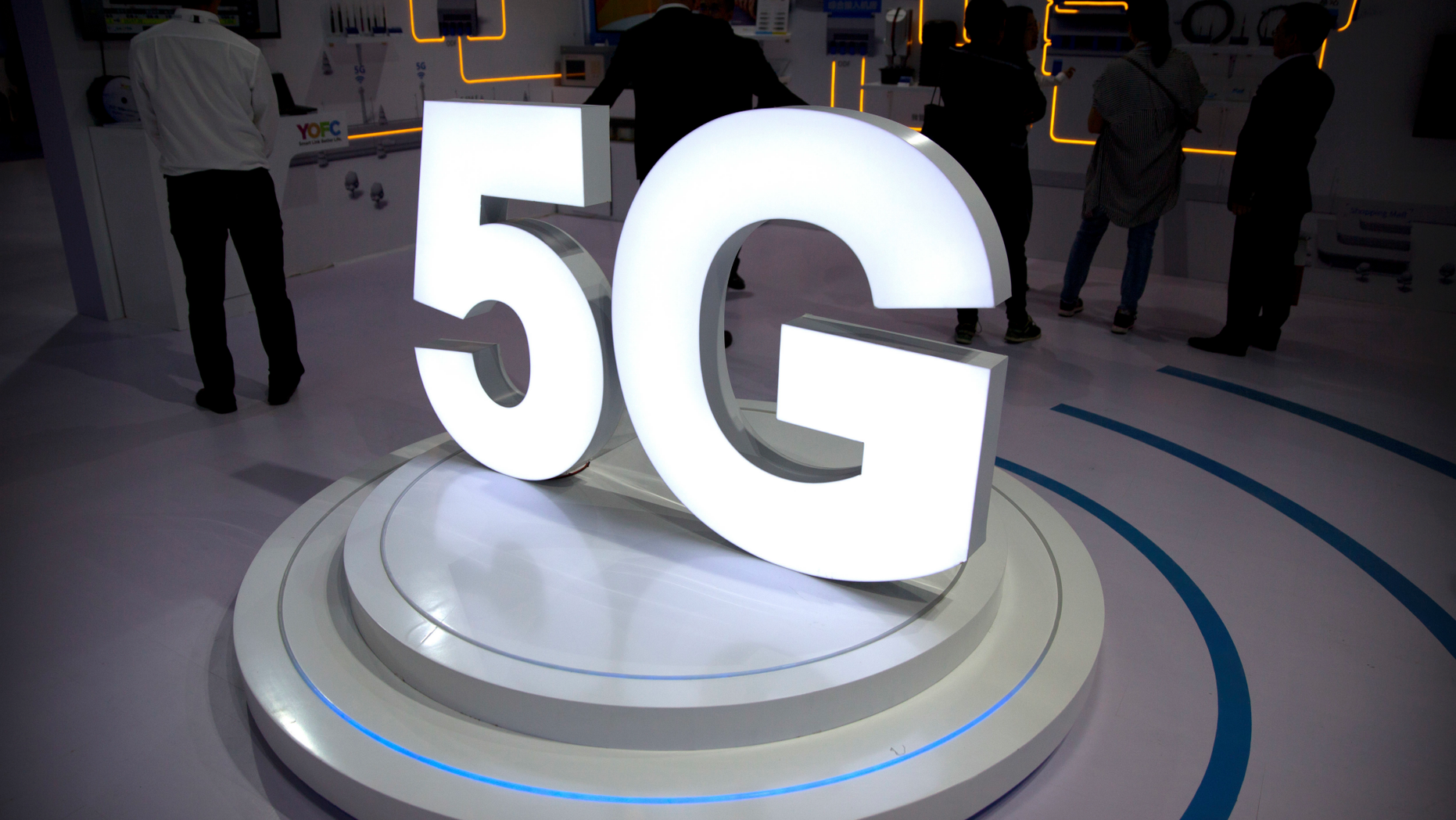 FILE- In this Sept. 26, 2018, file photo visitors stand near a 5G logo at a display the PT Expo in Beijing. Telecommunications equipment maker CommScope Holding Co. is paying about $5.7 billion for Arris International Plc. as it prepares for the entrance of faster 5G service to the wireless market. (AP Photo/Mark Schiefelbein, File)