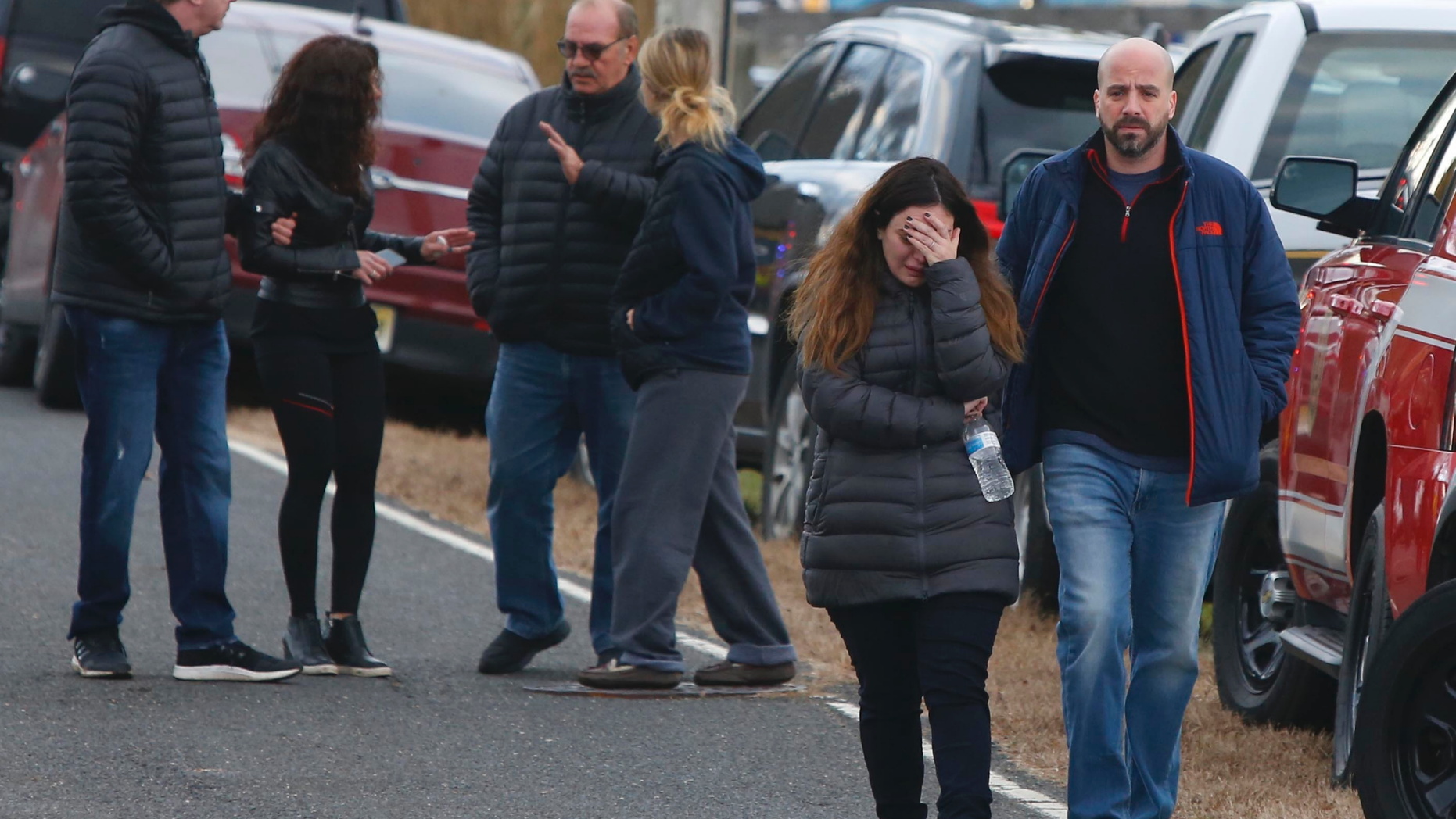 Pedestrians walk away from the scene of a fatal at 15 Willow Brook Rd. Tuesday, Nov. 20, 2018, in Colts Neck,N.J. Authorities say two adults and two children were found dead at the scene of a burning mansion near the New Jersey shore. Monmouth County prosecutor Christopher Gramiccioni says the fire continues to burn late Tuesday afternoon at the two-story home in Colts Neck. He says one body was found out front. He is not yet identifying the victims.(AP Photo/Noah K. Murray)