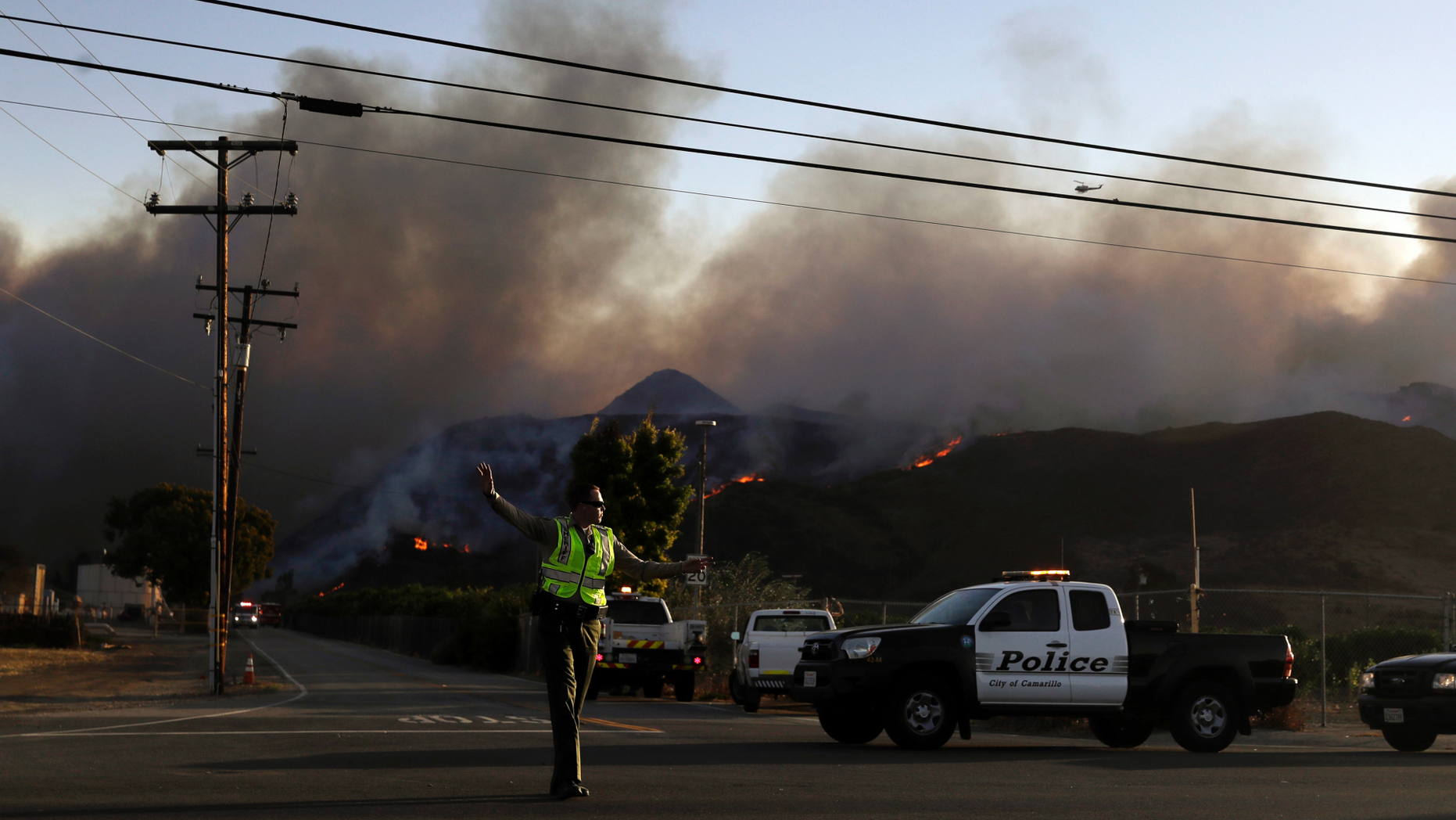 A police officer mans a checkpoint in front of an advancing wildfire Thursday, Nov. 8, 2018, near Newbury Park, Calif. The Ventura County Fire Department has also ordered evacuation of some communities in the path of the fire, which erupted a few miles from the site of Wednesday night's deadly mass shooting at a Thousand Oaks bar. (AP Photo/Marcio Jose Sanchez)