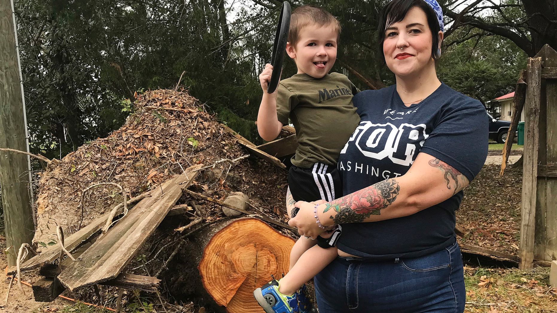 In this Oct. 25, 2018 photo, Lilly Langworth and her son Max stand in front of an oak tree felled by Hurricane Michael in the front yard of their Chipley, Fla., home. Langworth says she's watching for signs of trauma among her three children following the storm. (AP Photo/Tamara Lush)