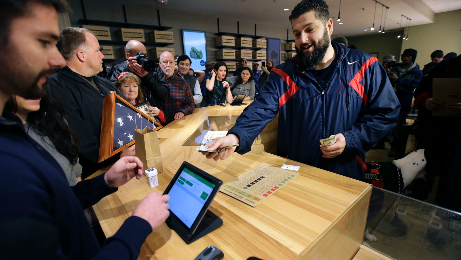 Stephen Mandile, right, an Iraq War veteran from Uxbridge, Mass., is the first to purchase recreational marijuana at the Cultivate dispensary on the first day of legal sales, Tuesday, Nov. 20, 2018, in Leicester, Mass. Cultivate is one of the first two shops permitted to sell recreational marijuana in the eastern United States, more than two years after Massachusetts voters approved it in 2016. (AP Photo/Steven Senne)