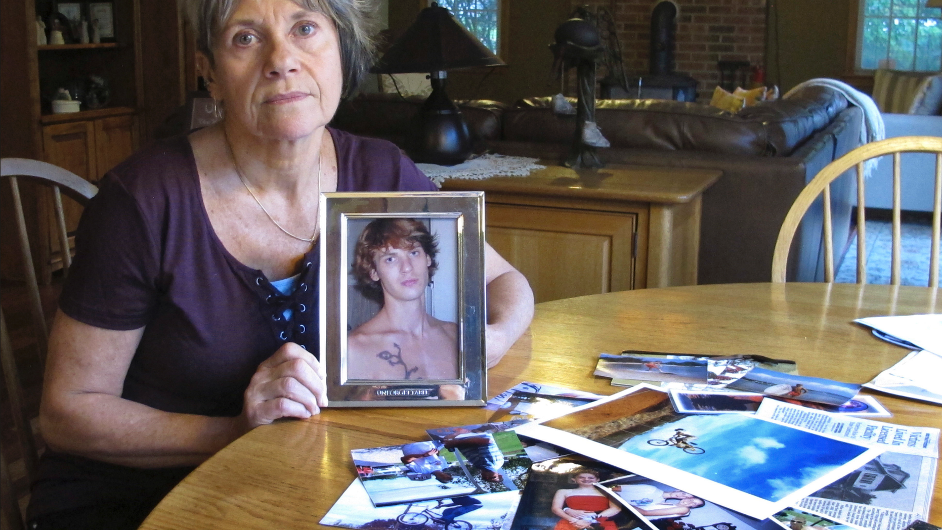In this Oct. 9, 2018 photo, Linda Marino poses with photographs of her son, Samuel, at her home in Tolland, Conn. Samuel Marino died in a 2009 car crash that relatives believe was intentional after becoming a victim of a male sex trafficking ring. Advocates are calling for more recognition and services for male victims. (AP Photo/Dave Collins)