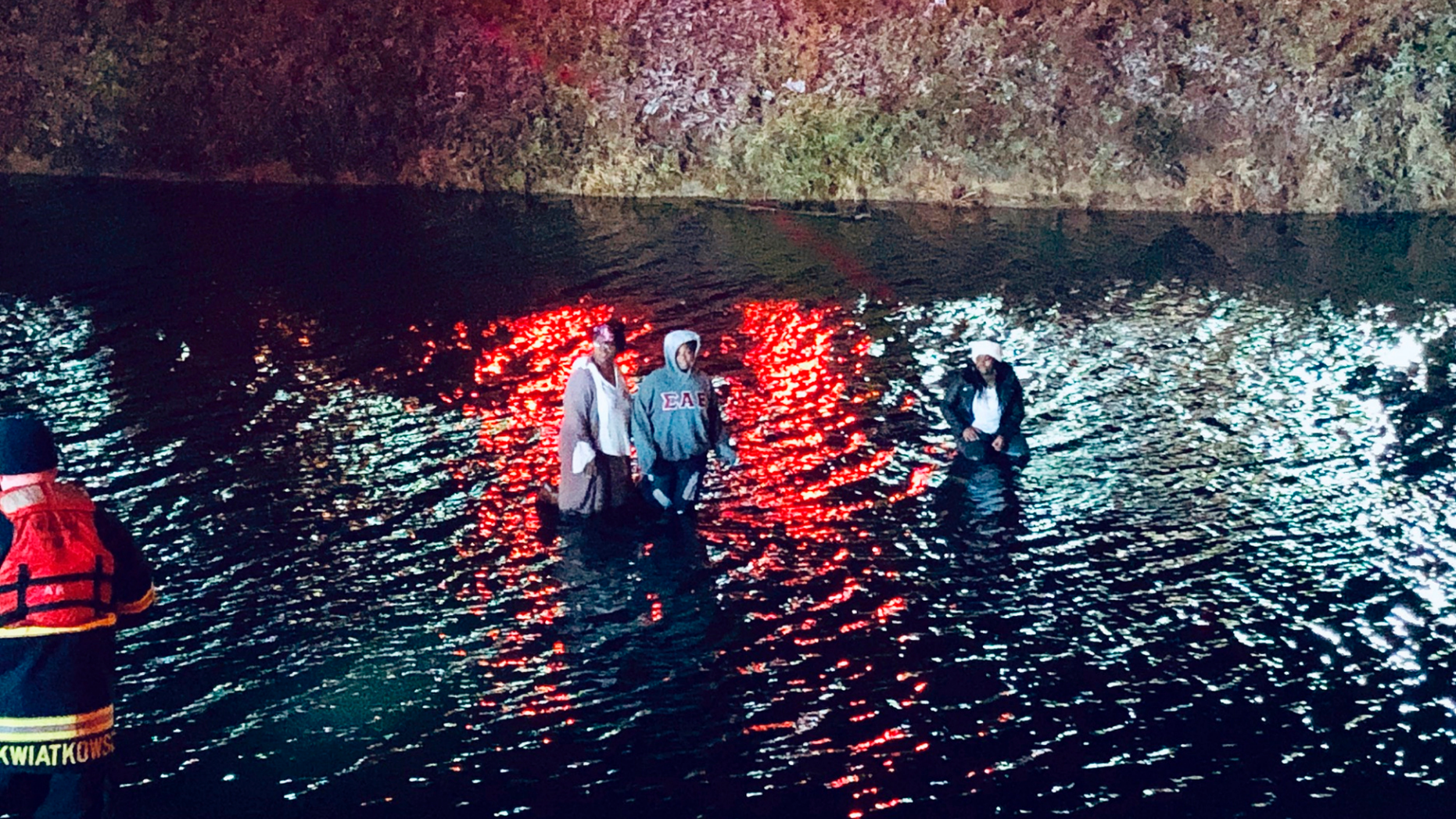In this Monday, Nov. 26, 2018, photo provided by the Indianapolis Fire Department, a mother, left, and her two daughters stand on top of their SUV after it slid from an icy bridge into the frigid water of a retention pond before fire department personnel rescued them in Indianapolis. A 4-year-old boy in the vehicle was rescued earlier by a passer-by. (Rita Reith/Indianapolis Fire Department via AP)