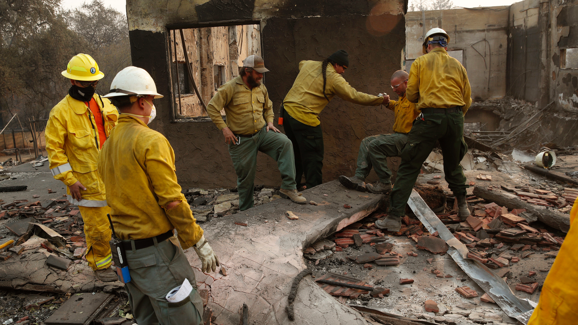 Fire crews clear rubble from the road near a building burned in the Camp Fire, Monday, Nov. 12, 2018, in Paradise, Calif. (AP Photo/John Locher)