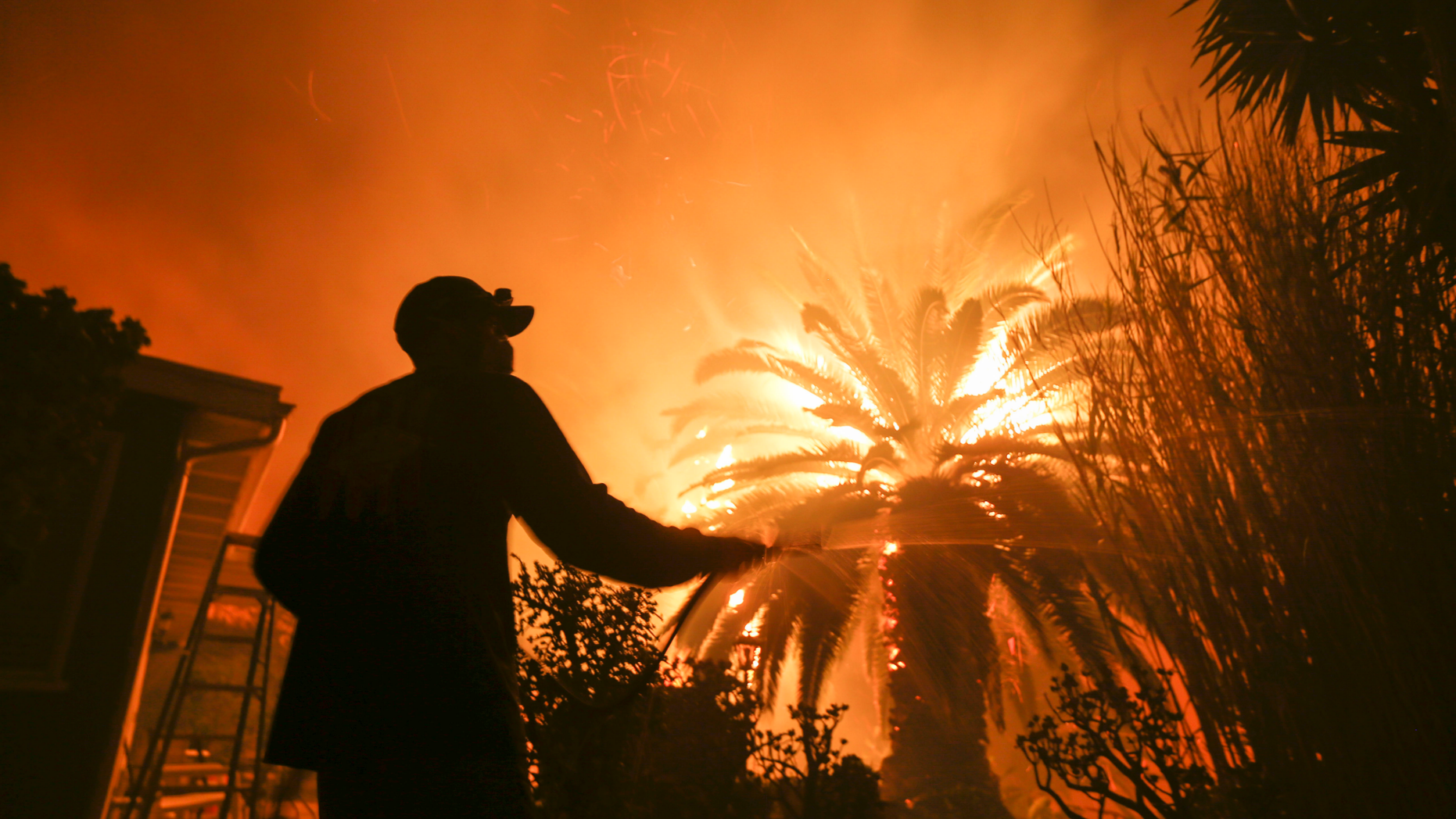Park Billow, 27, sprays water on the hot spots in his backyard as the Woolsey Fire burns in Malibu, Calif., Friday, Nov. 9, 2018. Authorities announced Friday that a quarter of a million people are under evacuation orders as wind-whipped flames rage through scenic areas west of Los Angeles and burn toward the sea. (AP Photo/Ringo H.W. Chiu)