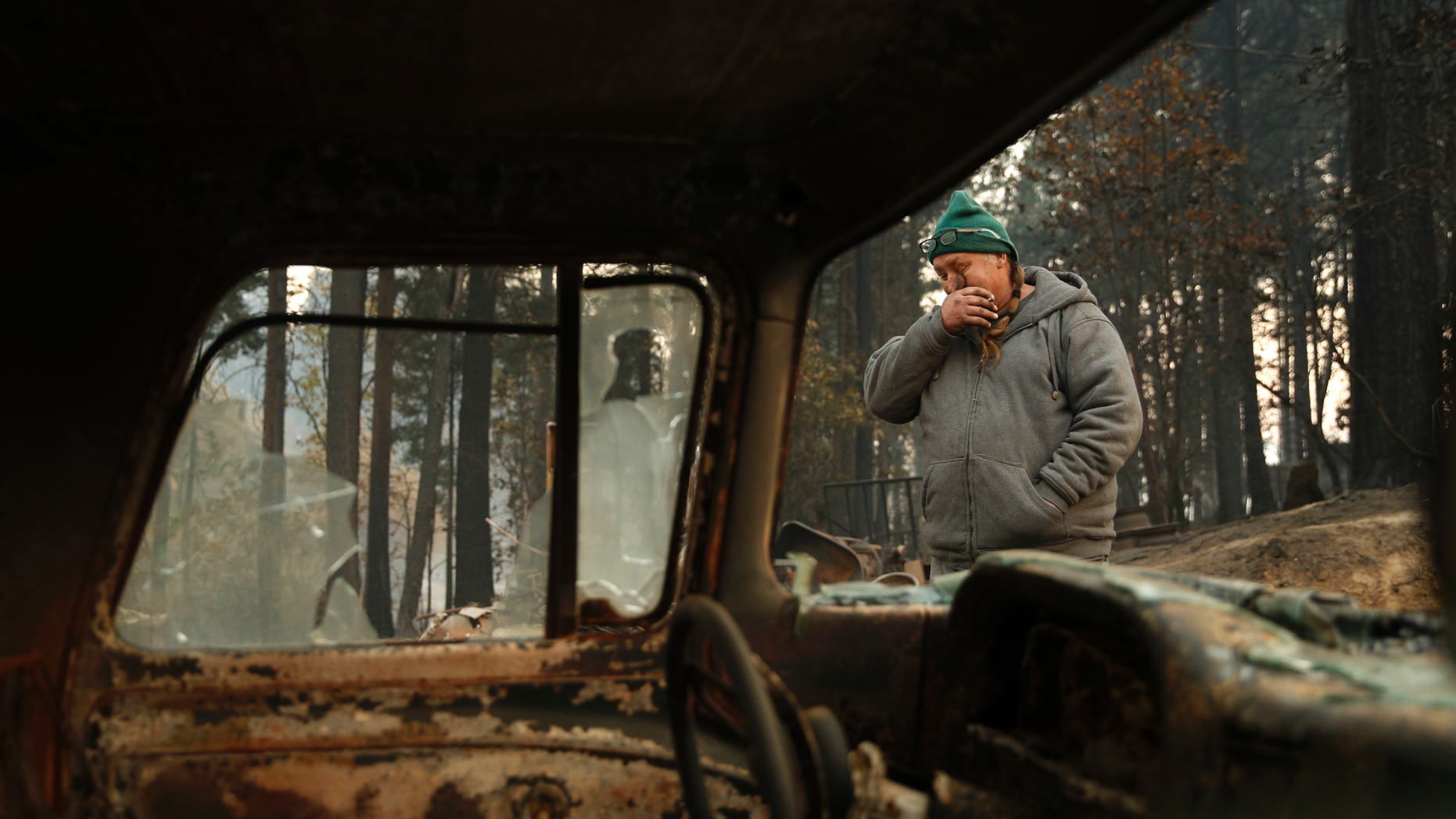 In this Nov. 15, 2018, photo, Troy Miller wipes his eyes as he walks beside a burned out car on his property in Concow, Calif. Miller said he tried to evacuate when the Camp Fire came roaring through the area, but had to turn back when the roads were blocked with debris and fire. A small group of residents who survived the deadly wildfire are defying evacuation orders and living in the burn zone. (AP Photo/John Locher)