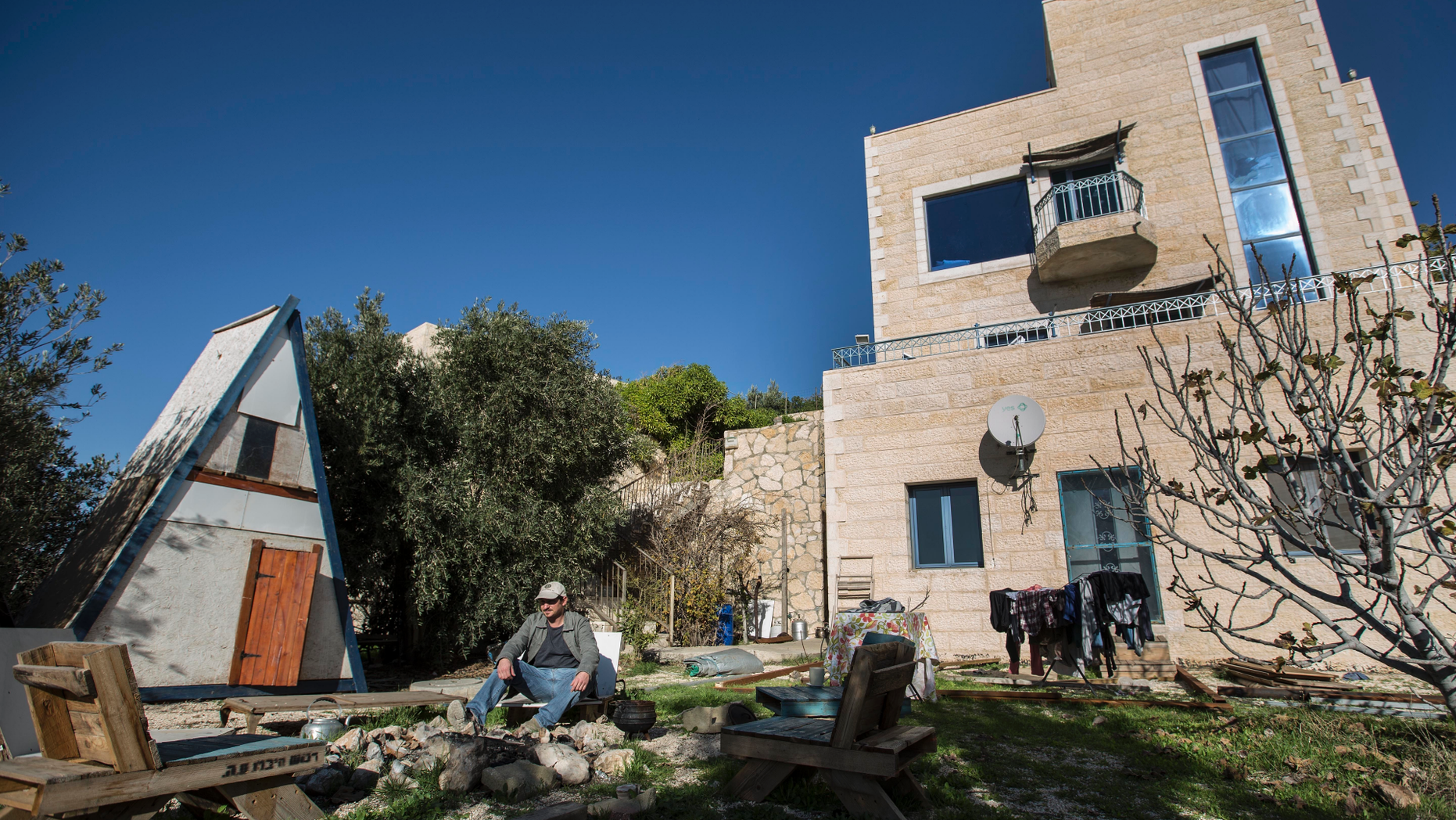 FILE - In this Jan. 17, 2016 file photo, Moshe Gordon sits outside his guest house advertised on the Airbnb international home-sharing site, in the Nofei Prat settlement in the West Bank. On Tuesday, Nov. 20, 2018, Israel's Tourism Minister Yariv Levin threatened the vacation rental company Airbnb with higher taxes, restrictions and legal repercussions over its decision to remove listings from Israeli settlements in the West Bank. (AP Photo/Tsafrir Abayov, File)