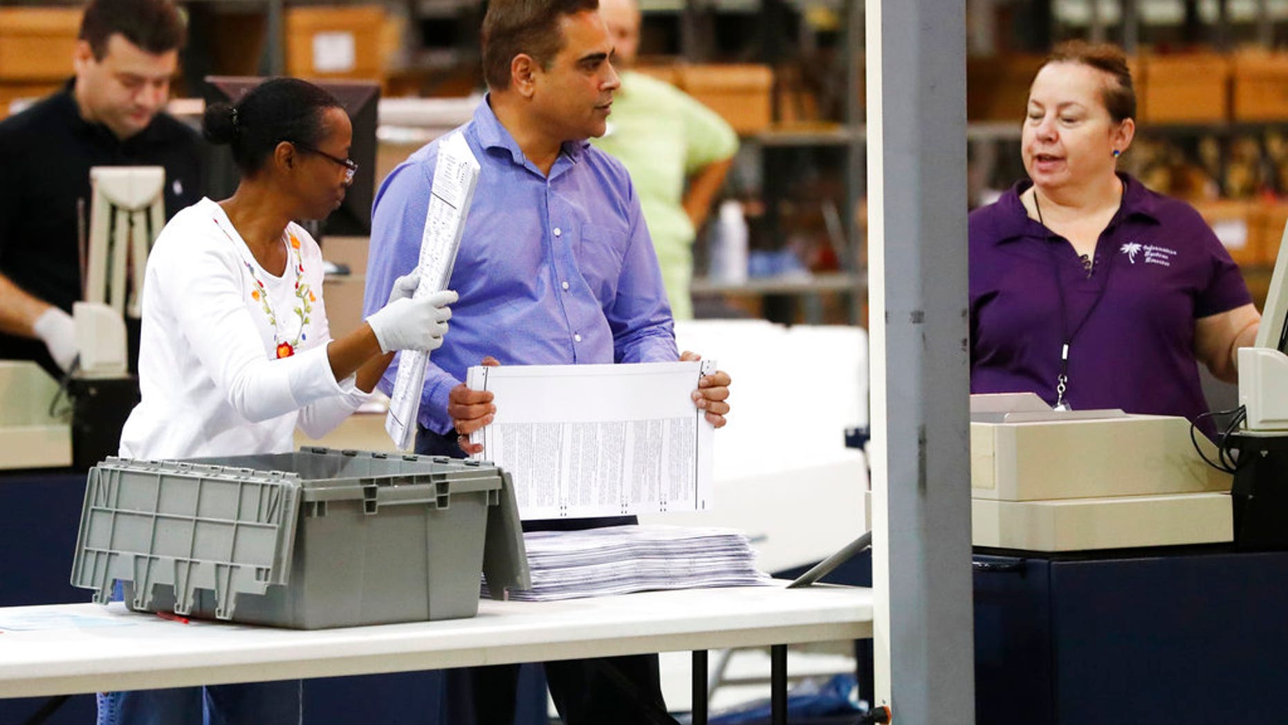 Employees at the Palm Beach County Supervisor of Elections office feed ballots through a machine as they count votes during a recount, Tuesday, Nov. 13, 2018, in West Palm Beach, Fla. (AP Photo/Wilfredo Lee)