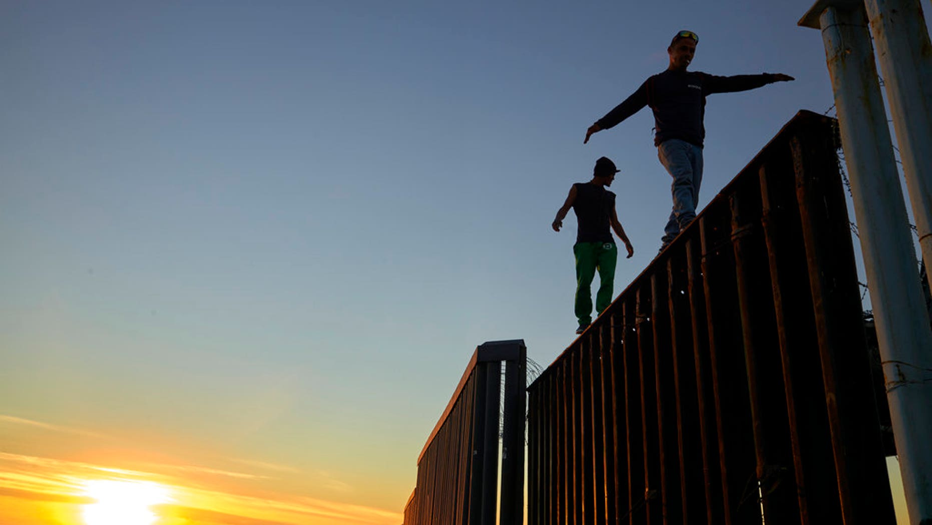 Two Central American migrants walk along the top of the border structure separating Mexico and the United States Wednesday, Nov. 14, 2018, in Tijuana, Mexico. Migrants in a caravan of Central Americans scrambled to reach the U.S. border, catching rides on buses and trucks for hundreds of miles in the last leg of their journey Wednesday as the first sizable groups began arriving in the border city of Tijuana. (AP Photo/Gregory Bull)