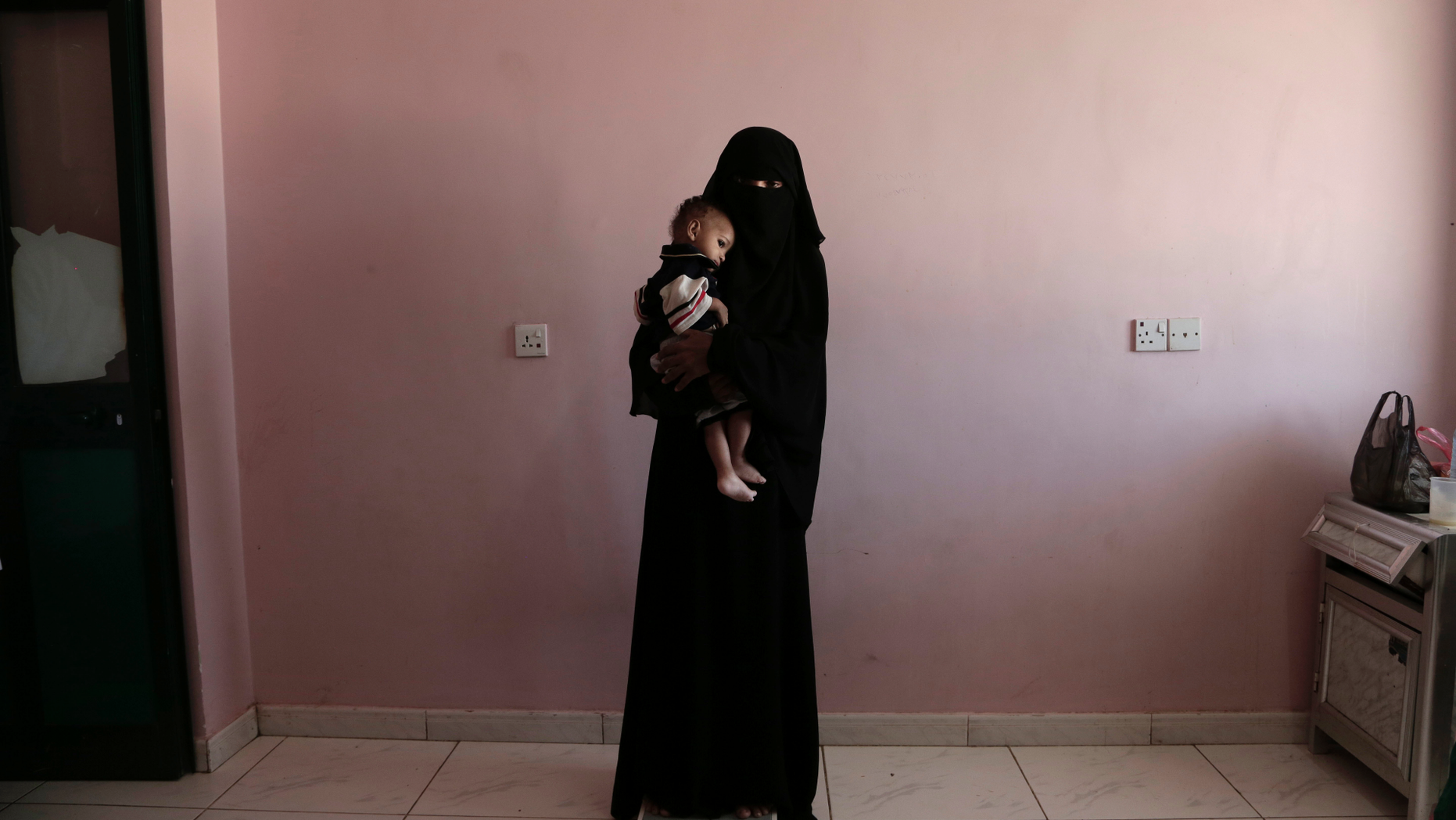 FILE - In this Feb. 13, 2018, file photo, Umm Mizrah, a 25-year-old Yemeni woman, holds her son Mizrah on a scale in Al-Sadaqa Hospital in the southern Yemen city of Aden. The woman, who is nearly into the second trimester of her pregnancy, weighed 38 kilograms (84 pounds), severely underweight. Mizrah, who was 17 months old, weighed 5.8 kilograms (12.8 pounds), around half the normal weight for his age. (AP Photo/Nariman El-Mofty, File)