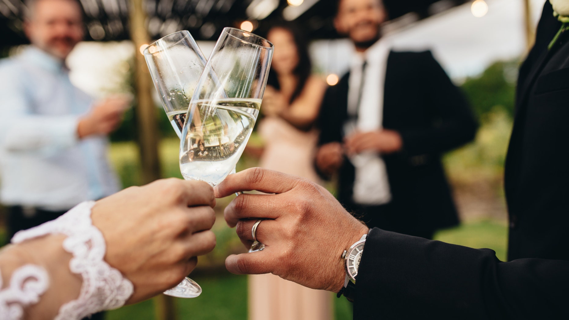 Close up of new married couple toasting champagne glasses at wedding party. Bride and groom hands clinking glasses at wedding reception.