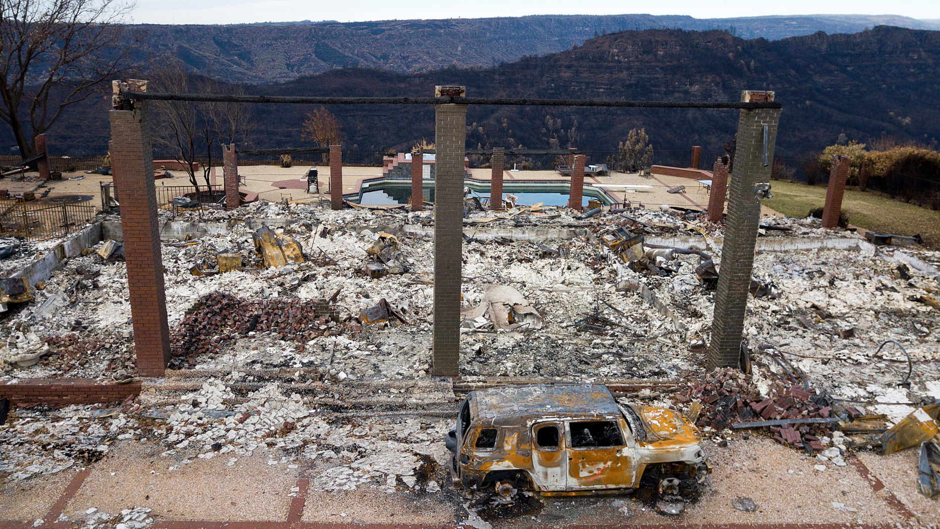 FILE - In this Dec. 3, 2018 file photo, a vehicle rests in front of a home leveled by the Camp Fire in Paradise, Calif. Authorities estimate it will cost at least $3 billion to clear debris of 19,000 homes destroyed by California wildfires last month. State and federal disaster relief officials said Tuesday, Dec. 11, 2018, that private contractors will most likely begin removing debris in January from Butte, Ventura and Los Angeles counties and costs are likely to surpass initial estimates. (AP Photo/Noah Berger, File)