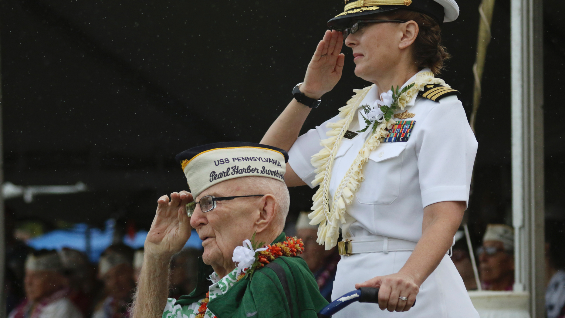Everett Hyland, seated, who survived the attack on Pearl Harbor as a crew member of the USS Pennsylvania, salutes along with his granddaughter Navy Cmdr. Anna-Marie Fine on Friday, Dec. 7, 2018 as the USS Michael Murphy passes in Pearl Harbor, Hawaii during a ceremony marking the 77th anniversary of the Japanese attack. The Navy and National Park Service jointly hosted the remembrance ceremony at a grassy site overlooking the water and the USS Arizona Memorial. (AP Photo/Audrey McAvoy)