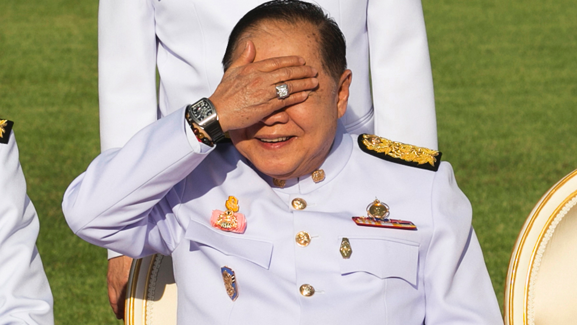 FILE - In this Dec. 4, 2017, file photo, Thailand's Deputy Prime Minister Prawit Wongsuwan raises his hand to shade his eyes from the sun while wearing a luxury watch and diamond ring during an official ceremony at the Government House. Thailand's National Anti-Corruption Commission has declared Prawit innocent of failing to declare his assets in a case that sparked a scandal when he was spotted wearing a number of luxury watches that he would not easily be able to afford on his government salary. (AP Photo/Krit Phromsakla Na Sakolnakorn, File)