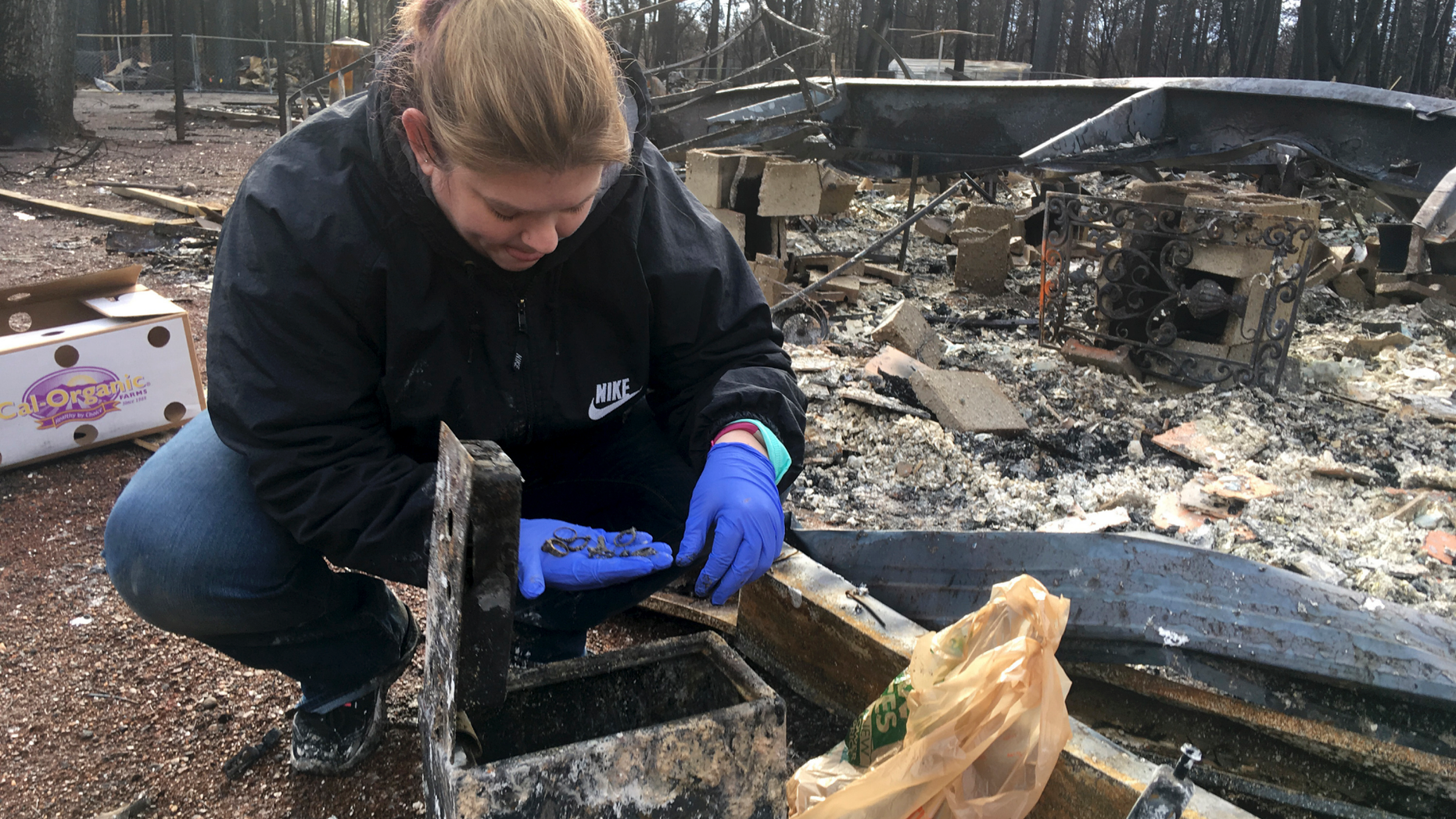 In this photo taken Wednesday, Dec. 5, 2018 Jennifer Christensen sorts through items found in a safe at the remains of her home in Paradise, Calif. Christensen and her 2-year-old son, Avery, moved to Paradise about a year ago. Upon returning to what was once home, she found a safe with melted jewelry in it. Christensen is not sure of her future plans but feels so much loyalty to her town that she recently had a tattoo done on her upper arm that reads, "Love is thicker than smoke," and below that, "Paradise Strong." (AP Photo/Don Thompson)