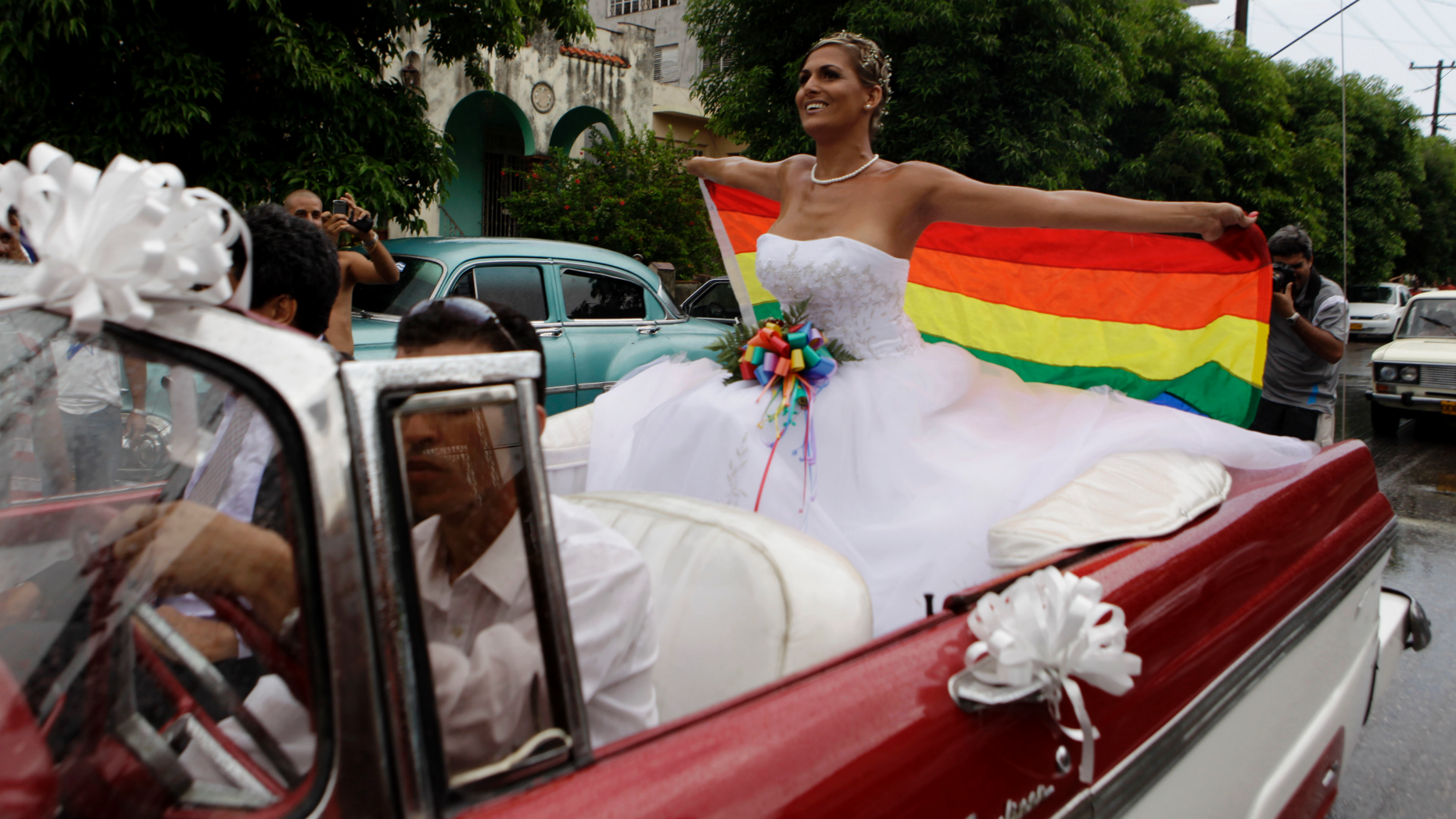 FILE - In this Aug. 13, 2011 file photo, holding up a gay pride flag, transsexual Wendy Iriepa, who had a sex change, rides to her wedding on a classic car in Havana, Cuba. Cuba said on Tuesday, Dec. 18, 2018 that language promoting the legalization of gay marriage will be removed from the draft of a new constitution after widespread popular rejection of the idea. (AP Photo/Javier Galeano, File)