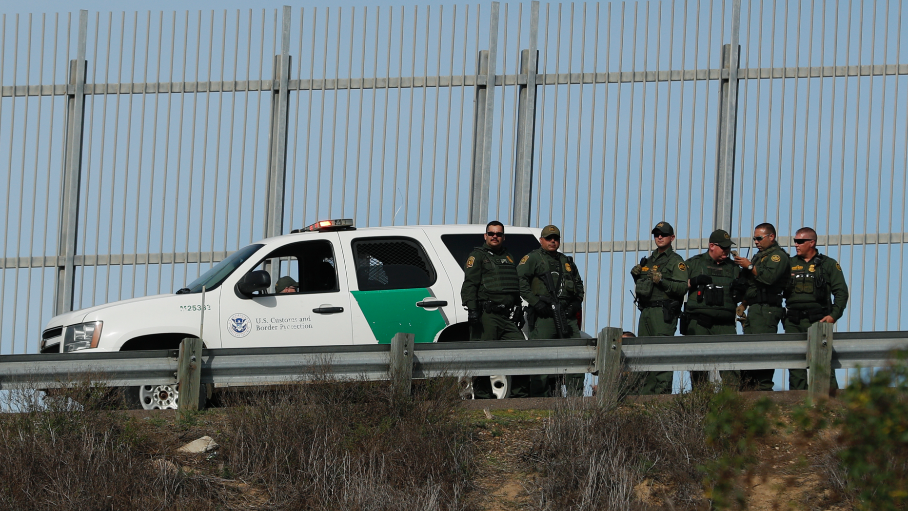 U.S. Border Patrol agents stand in front of a secondary fence in San Diego, California looking across border wall toward Mexico as they respond to a group of Central American migrants who crossed the border wall illegally, seen from across the wall in Tijuana, Mexico, Sunday, Dec. 9, 2018. Discouraged by the long wait to apply for asylum through official ports of entry, many Central American migrants from recent caravans are choosing to cross the U.S. border wall illegally and hand themselves in to Border Patrol agents to request asylum. (AP Photo/Rebecca Blackwell)