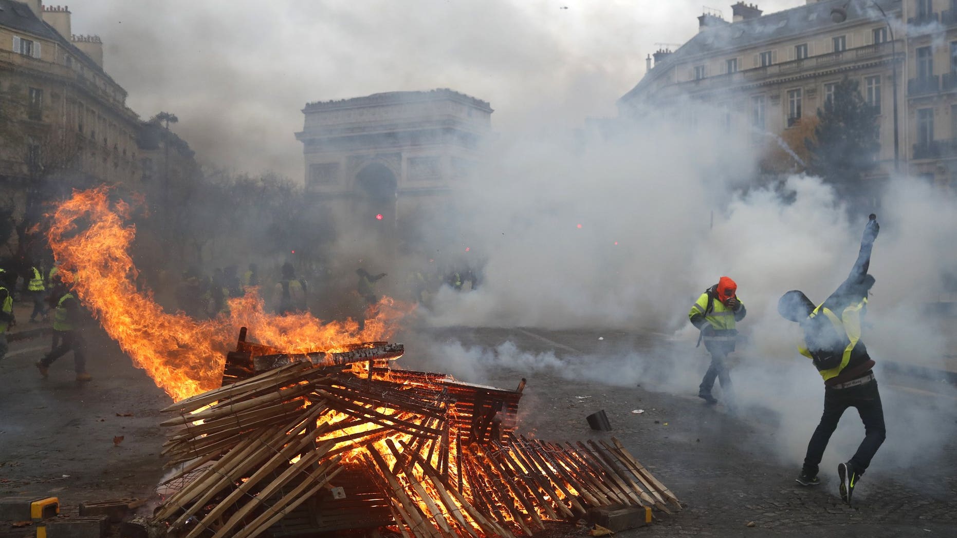 Demonstrators run by a burning barricade near the Arc de Triomphe during a demonstration Saturday, Dec.1, 2018 in Paris.