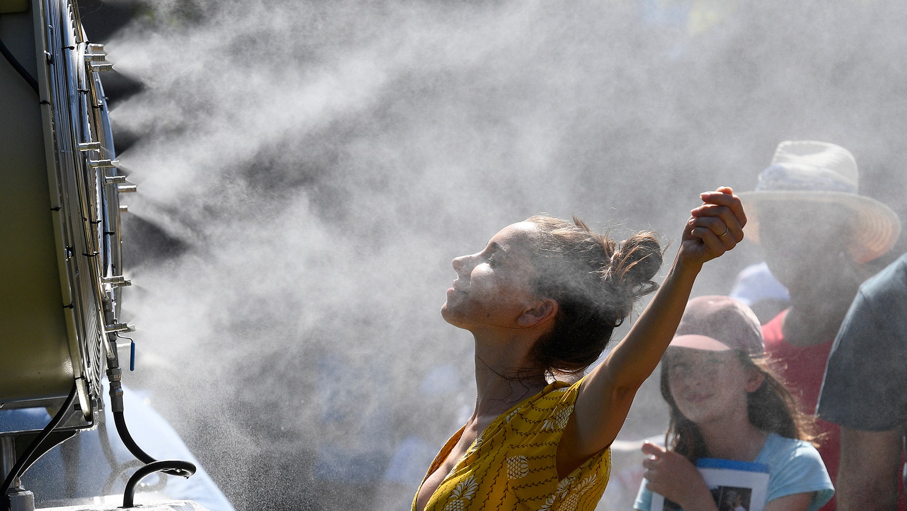 Spectators cool themselves down with a water mist fan during play on day one at the Australian Open tennis championships in Melbourne, Australia, Monday, Jan. 14, 2019.